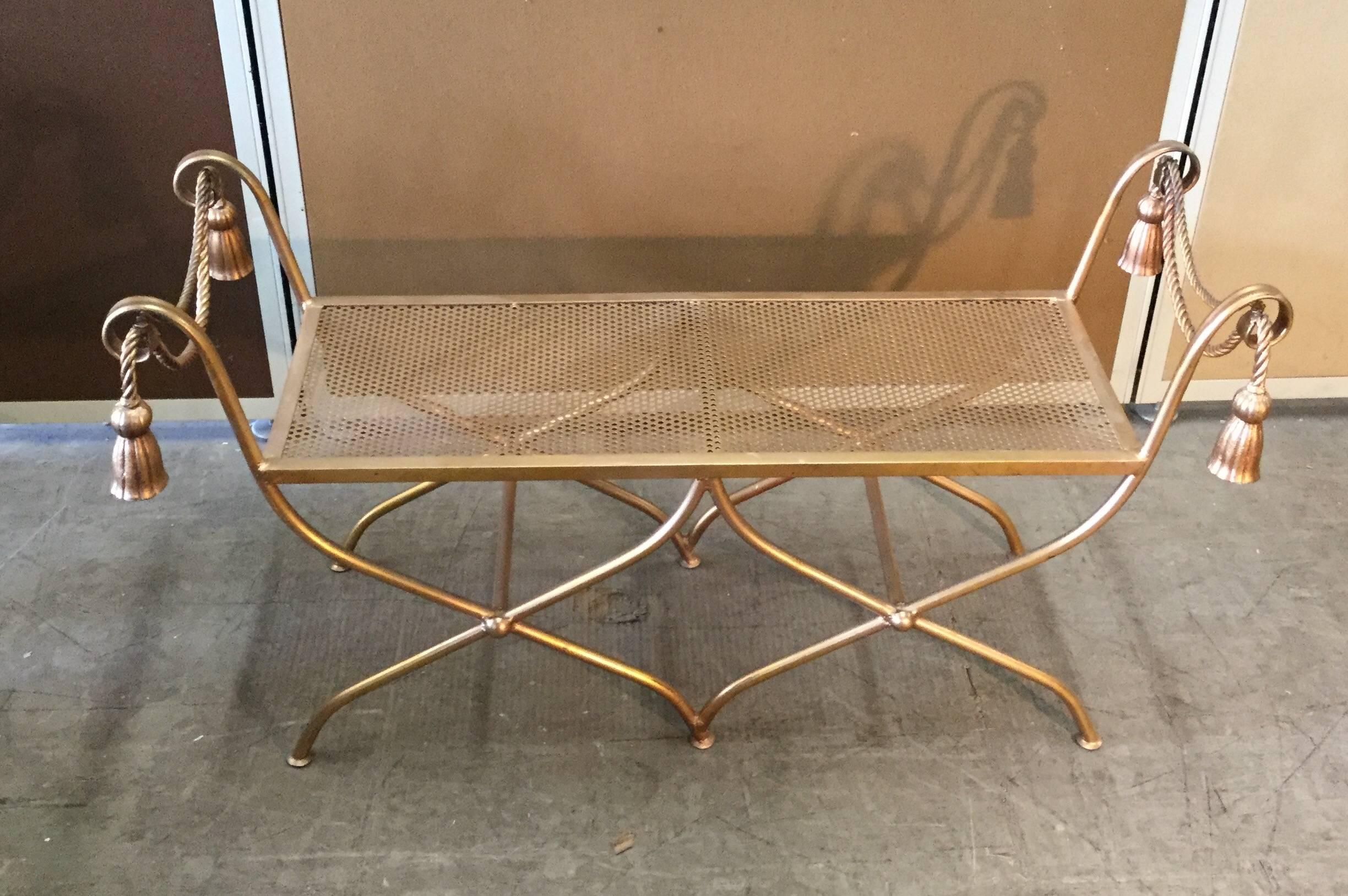 A fanciful gilt iron bench with criss crossed legs, expanded wire deck and rope and tassel decorations. Italian, circa 1970.