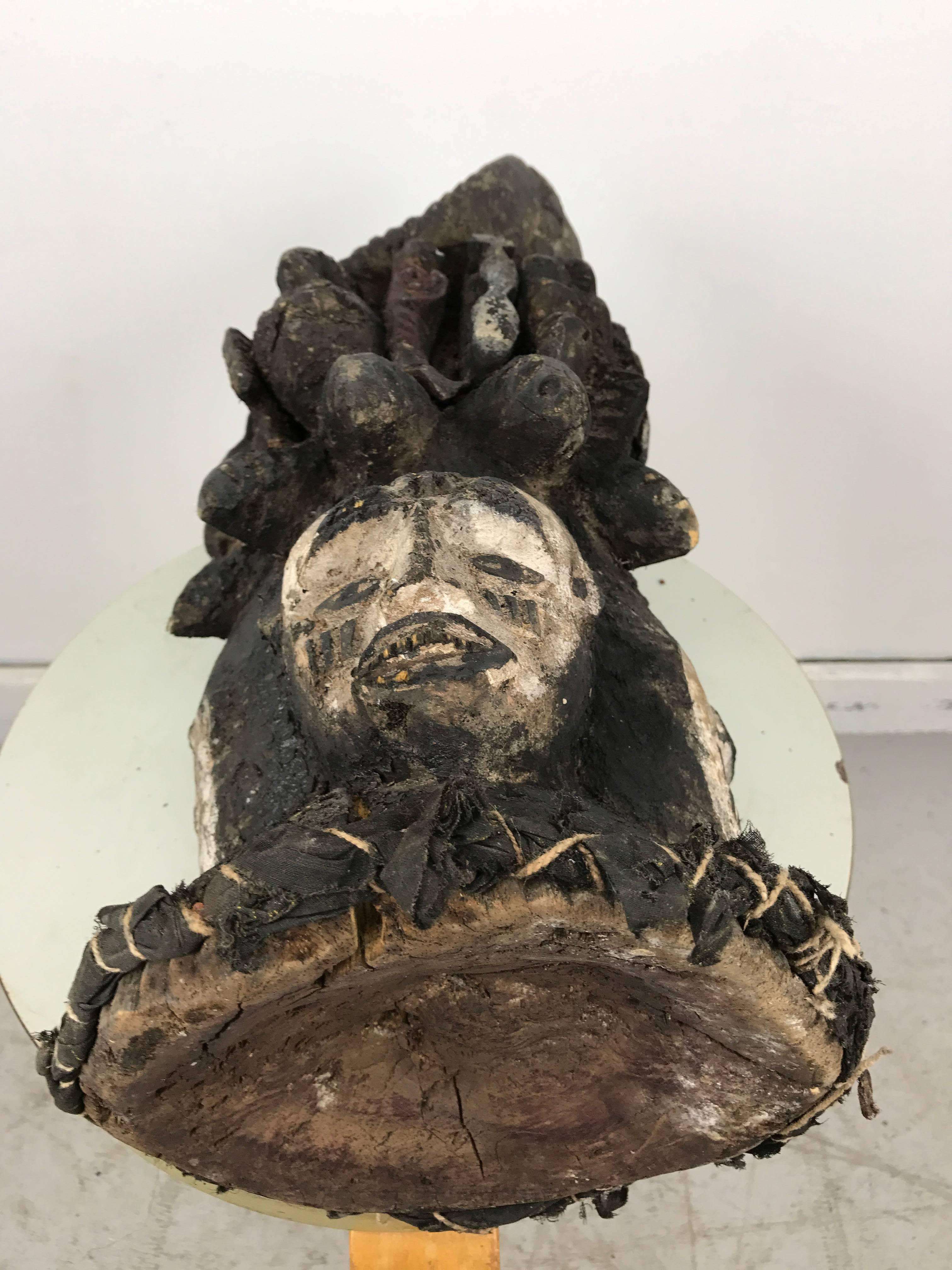 A fine Idoma Headdress, ungulali, rising from a flaring conical base with holes around the rim for attachment, the first tier of three stylized faces with tapering chins, parted lips, pointed noses and cresent shaped eyes beneath arching brows, fine
