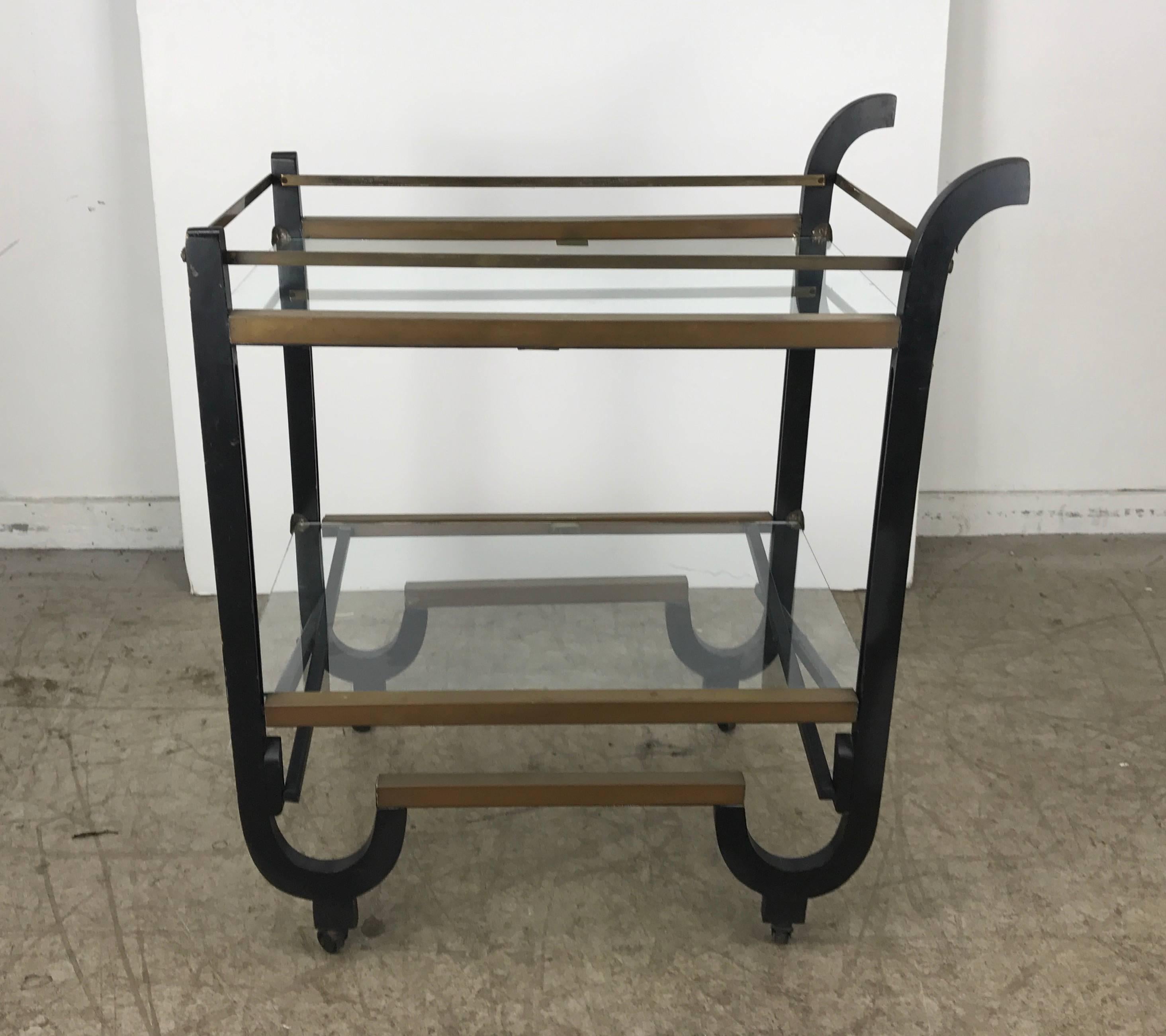 Stunning Art Deco brass and black lacquer bar or tea cart, attributed to Donald Deskey.

Sleek, Classic Deco design. Lacquered wood brass trim detailing and glass shelves. Collapsible construction for convenient storage as needed.