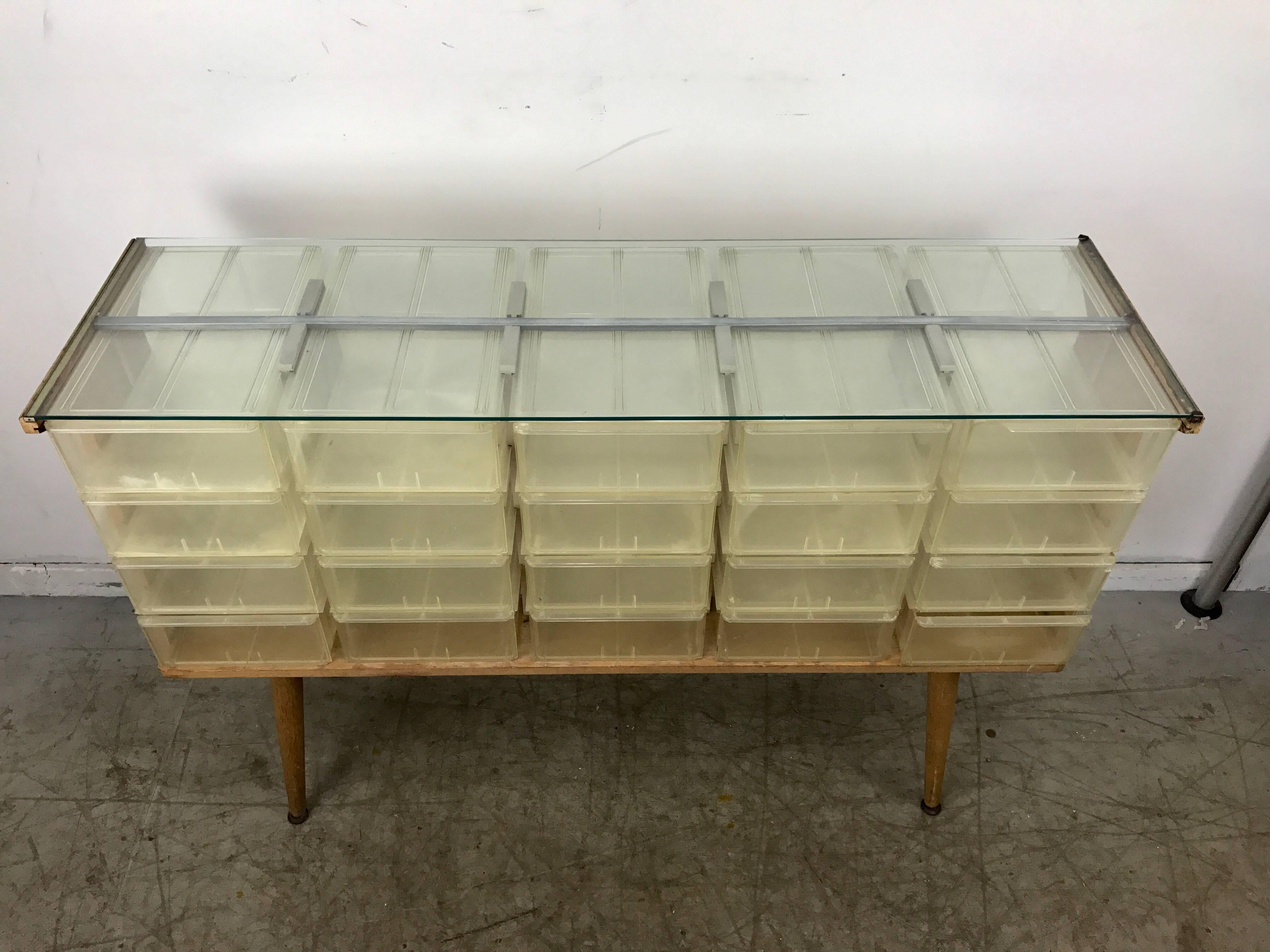 Unusual Mid-Century Modern store fixture featuring twenty polypropylene slide out drawers or cubbies encased in a classic cerused oakwood frame. Original glass top. Hand delivery avail to New York City or anywhere en route from Buffalo New York.