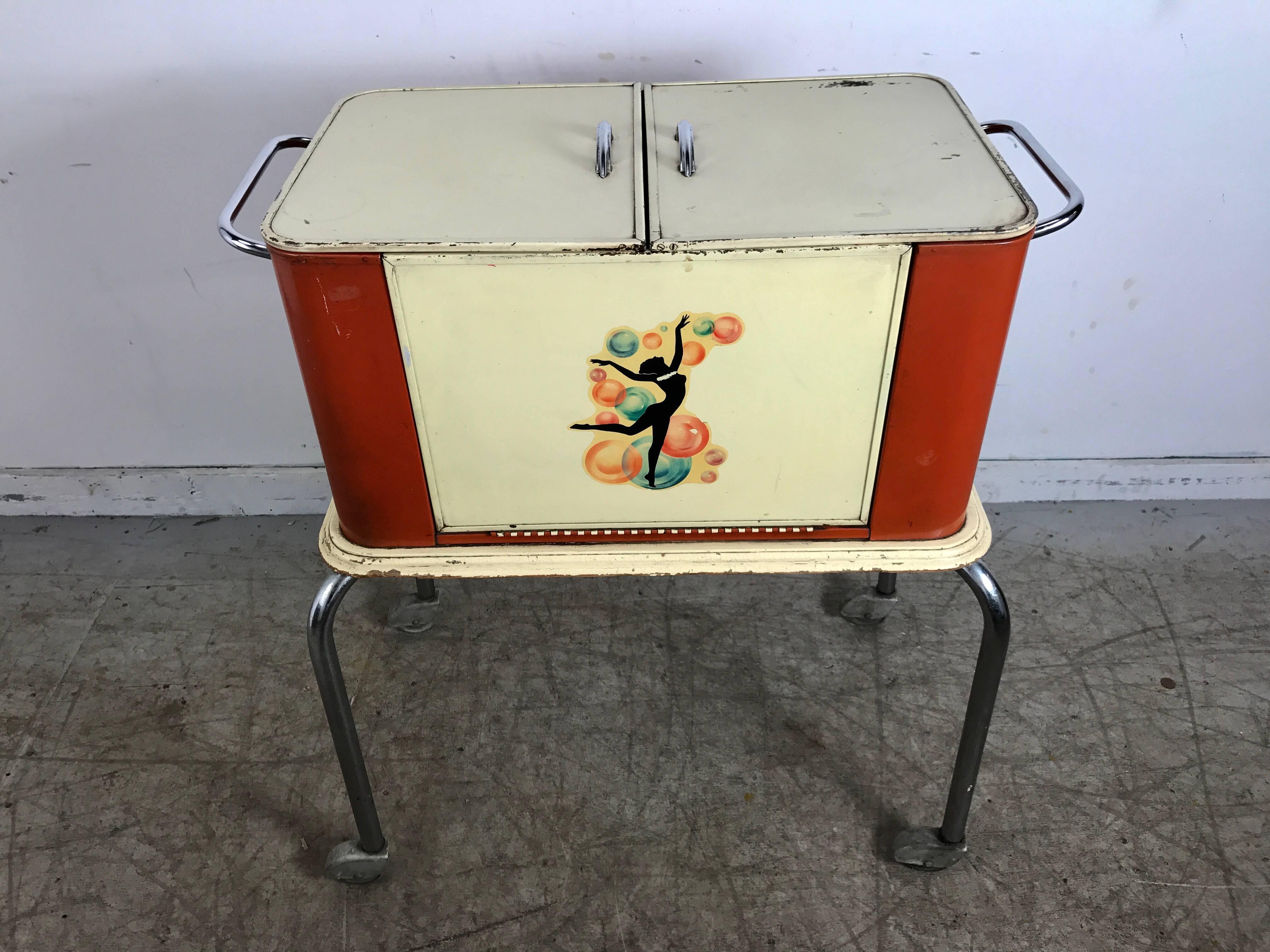 Stylized Art Deco portable dry bar, great little item. Rounded cabinet unfolds into a perfect portable server, tubular chrome base with skirted fender wheels, retains original iconic dancing woman graphic, bar when open measures 48.5 inches wide.