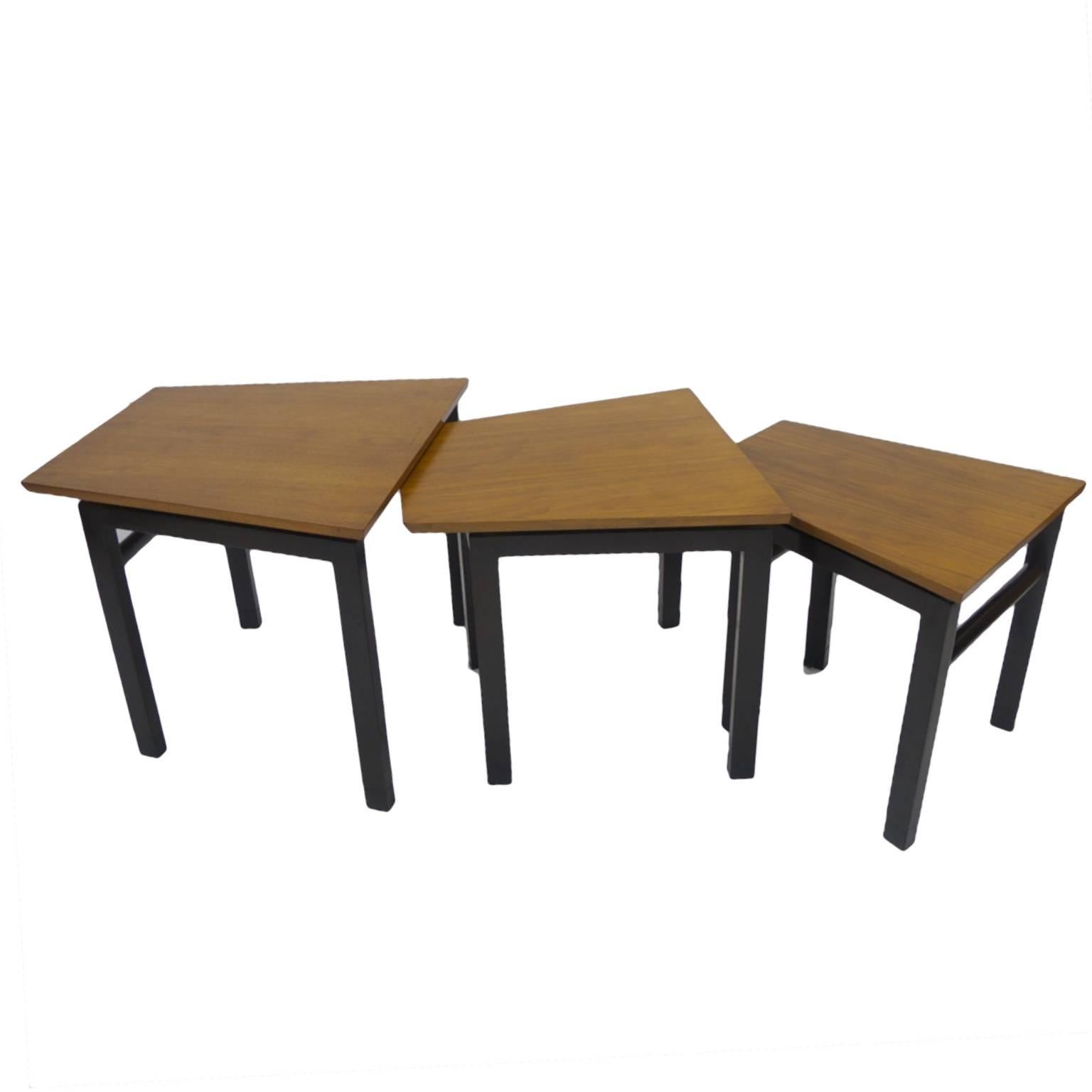 Stunning set of three sturdy trapezoid shaped nesting tables designed by Edward Wormley for Dunbar. Tops are constructed of walnut with a beautifully beveled edge for a streamlined look. Bases have an ebonized finish and each leg is capped with a