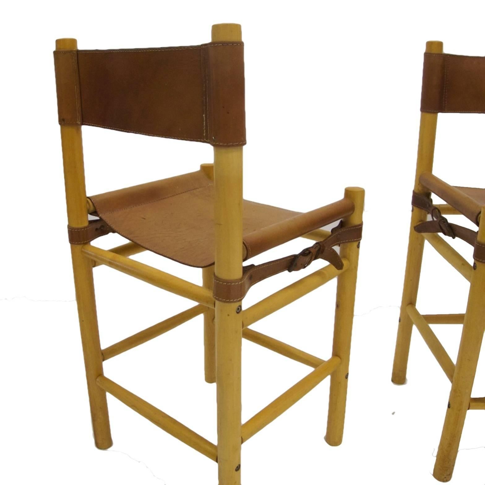A set of three bar stools in beech and heavy stitched leather. Side buckle detail. Versatile stools are perfect for modern decor or farm house. Leather is stamped Argentina.