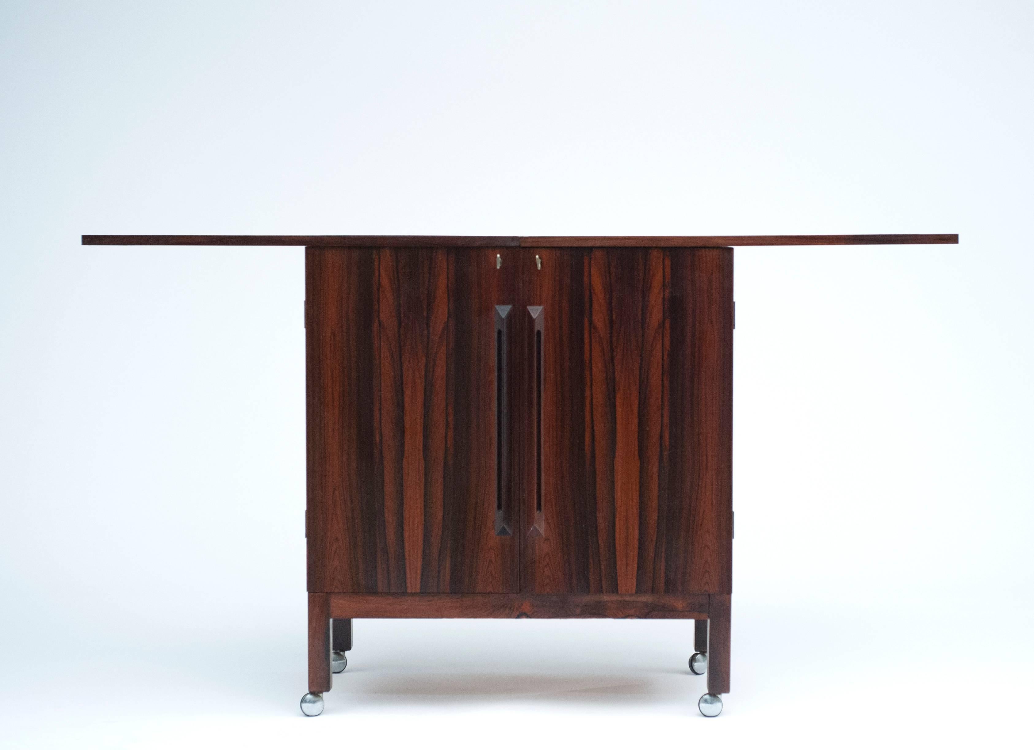 Desirable rosewood bar cabinet designed by Torbjørn Afdal for Bruksbo of Norway. Locking cabinet opens to reveal storage for all necessary bar accoutrements. Black laminate flip-top doubles in size for additional working space. Bar is complete with