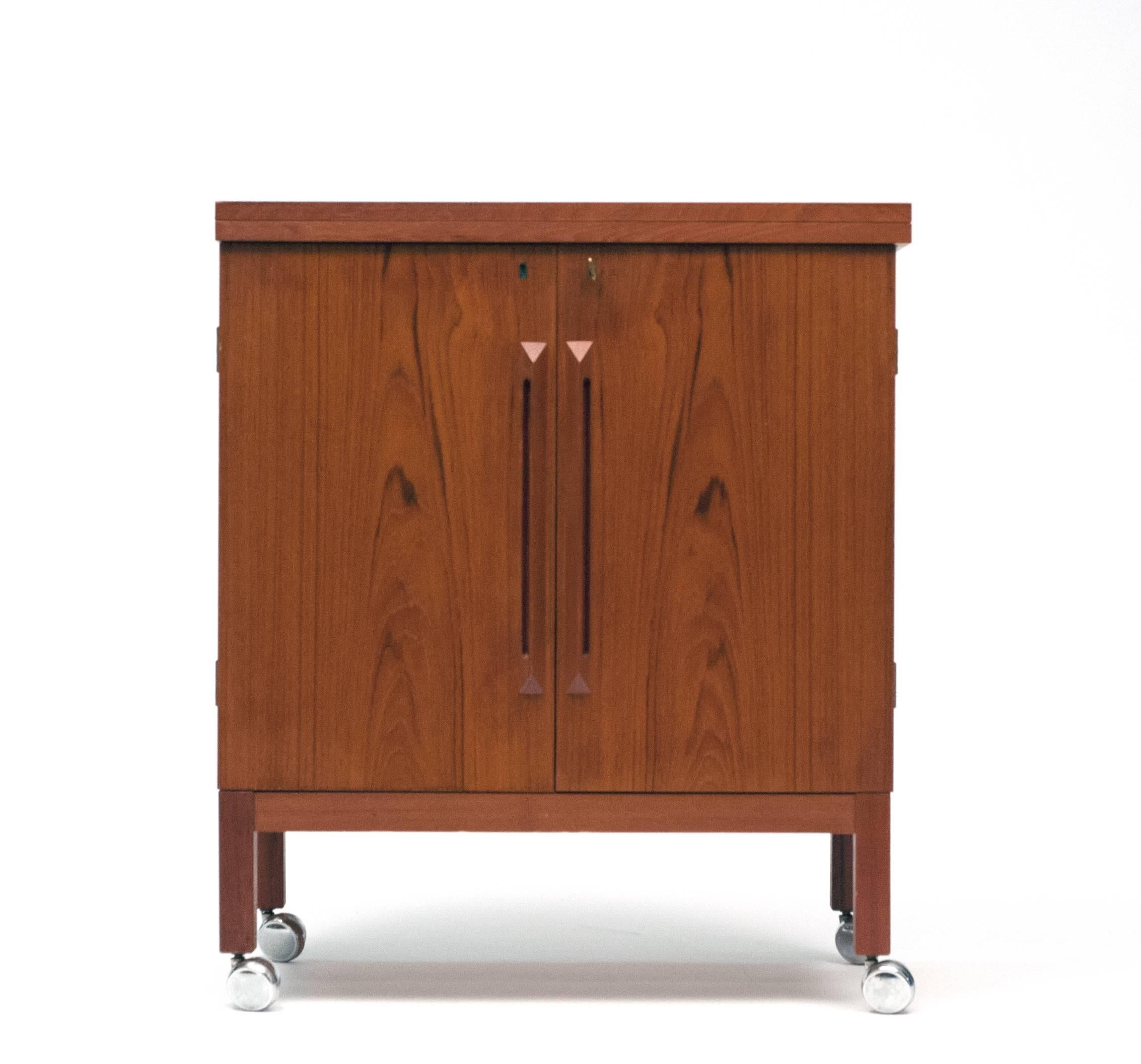 Attractive and functional flip-top bar cabinet in teak. High quality construction throughout. Locking cabinet opens to reveal storage for all necessary bar accoutrements. Black laminate flip-top is in excellent condition and measures 60.5 W x 16.5 D