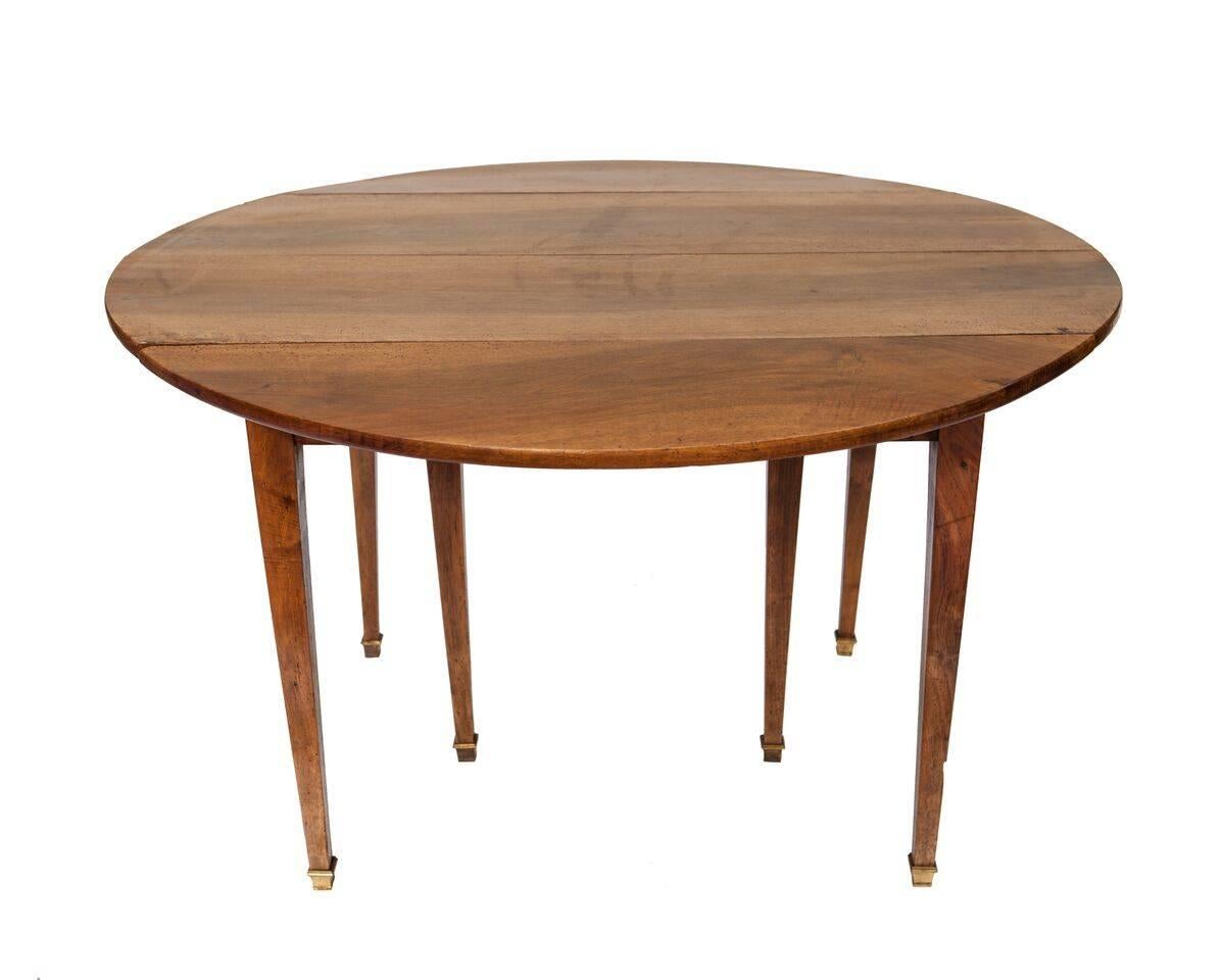 This French walnut drop-leaf table from the early 20th century features an oval top equipped with two drop leaves and one separable leaf. The table is raised on thin tapered legs with brass spade feet. Simple and sophisticated, there’s always a use