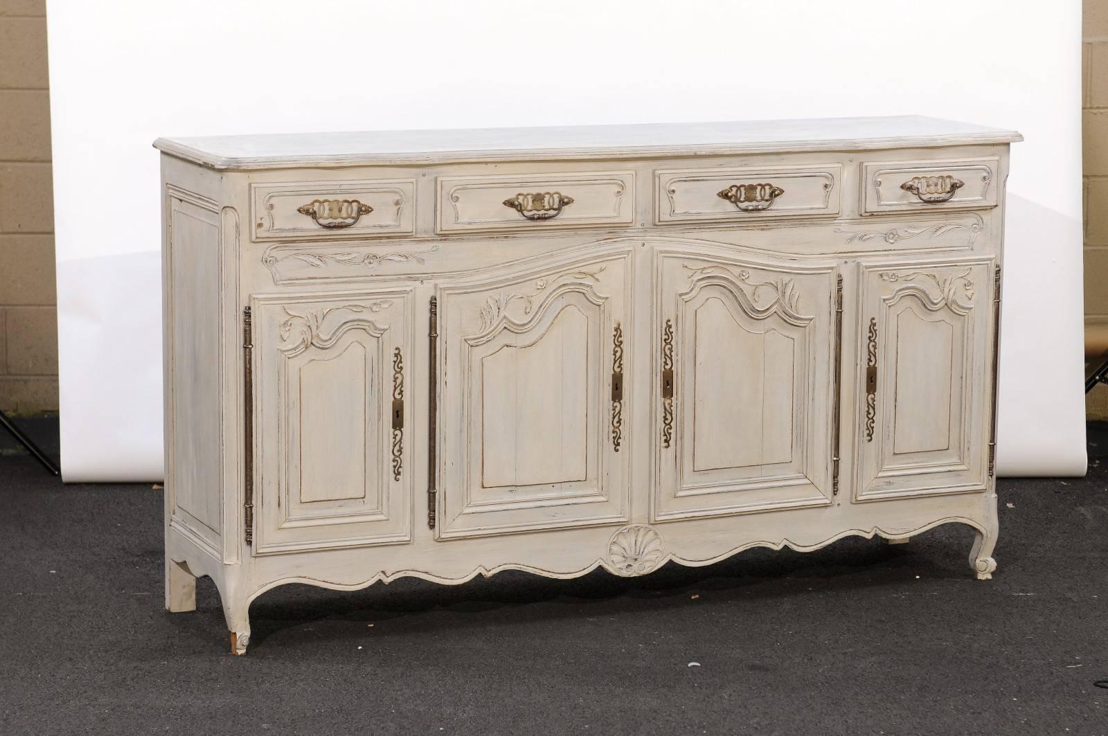 This French Louis XV style painted wood enfilade features a light color finish and four drawers over four doors decorated with delicately carved foliage motifs. The sinuous lines of the central panels echo the nice scalloping of the skirt, adorned