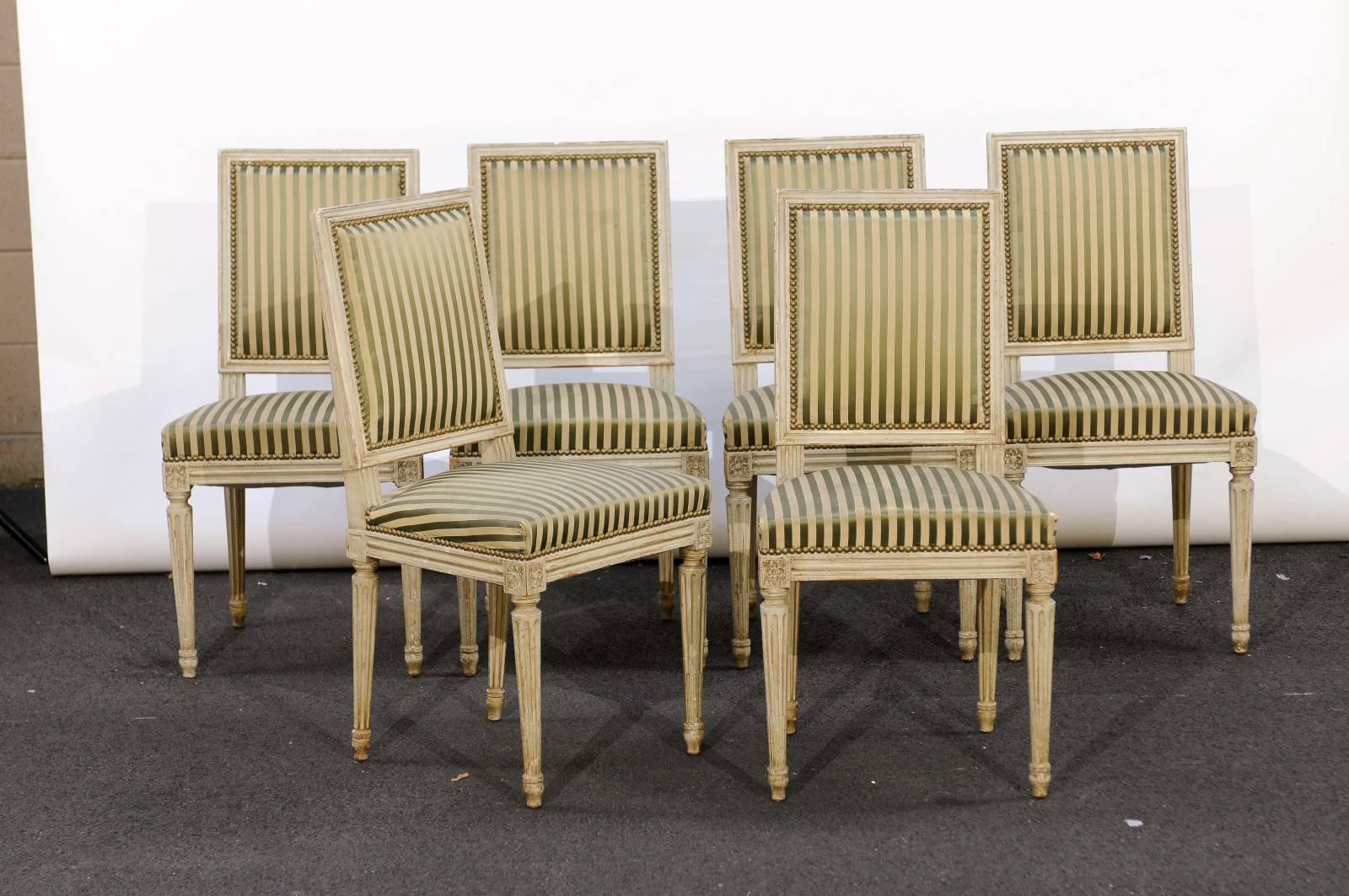 A set of six French Louis XVI style upholstered dining room side chairs with old paint, slanted rectangular backs, fluted and tapered legs and carved rosettes on the knees from the early 20th century. Pretty… oh so pretty! That’s how we felt about