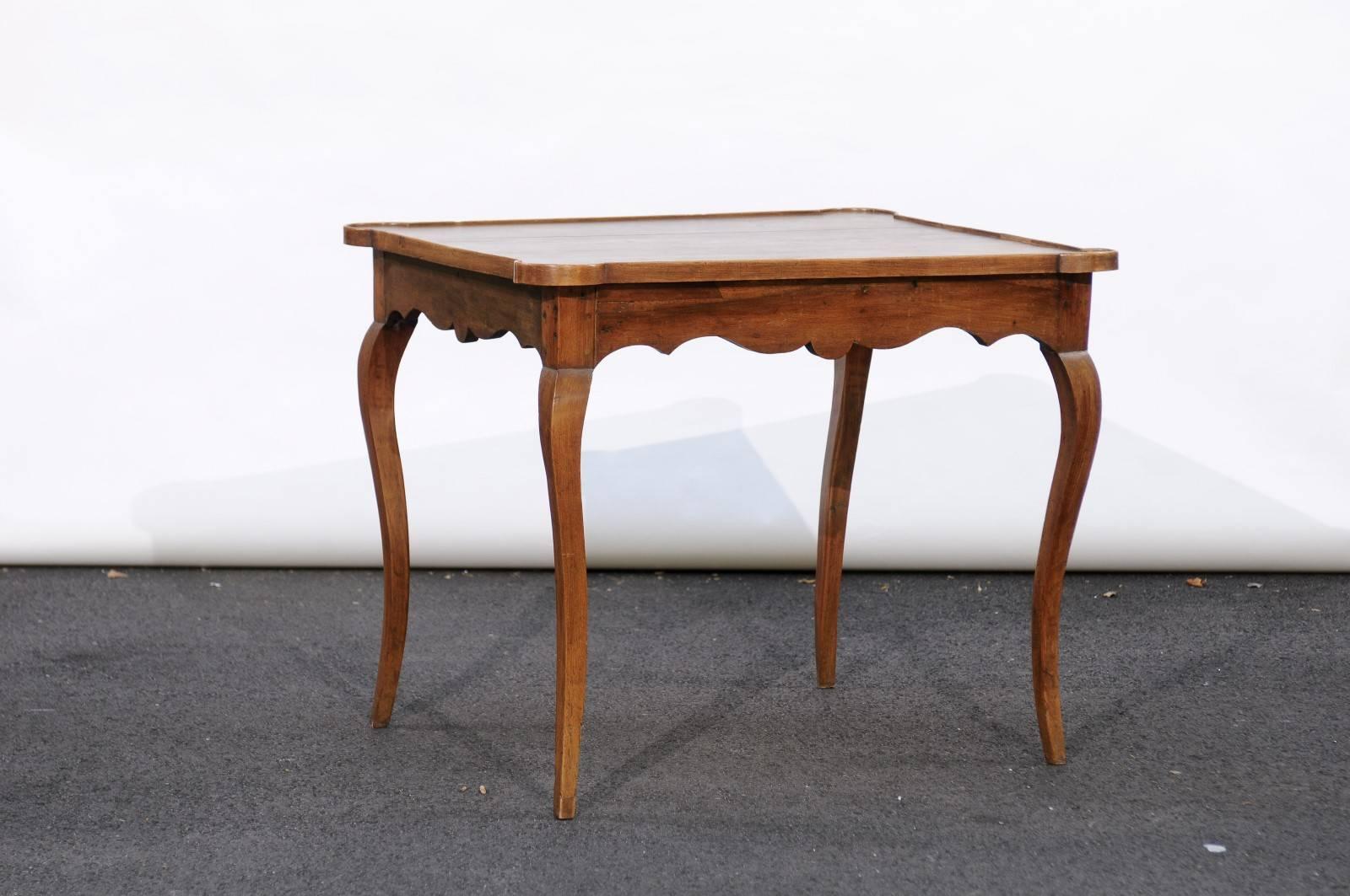 This French Louis XV style walnut game table from the late 19th century features a rectangular top with rounded corners over a beautifully scalloped apron, raised on four slender cabriole legs. A rich walnut patina combined with graceful curvy lines