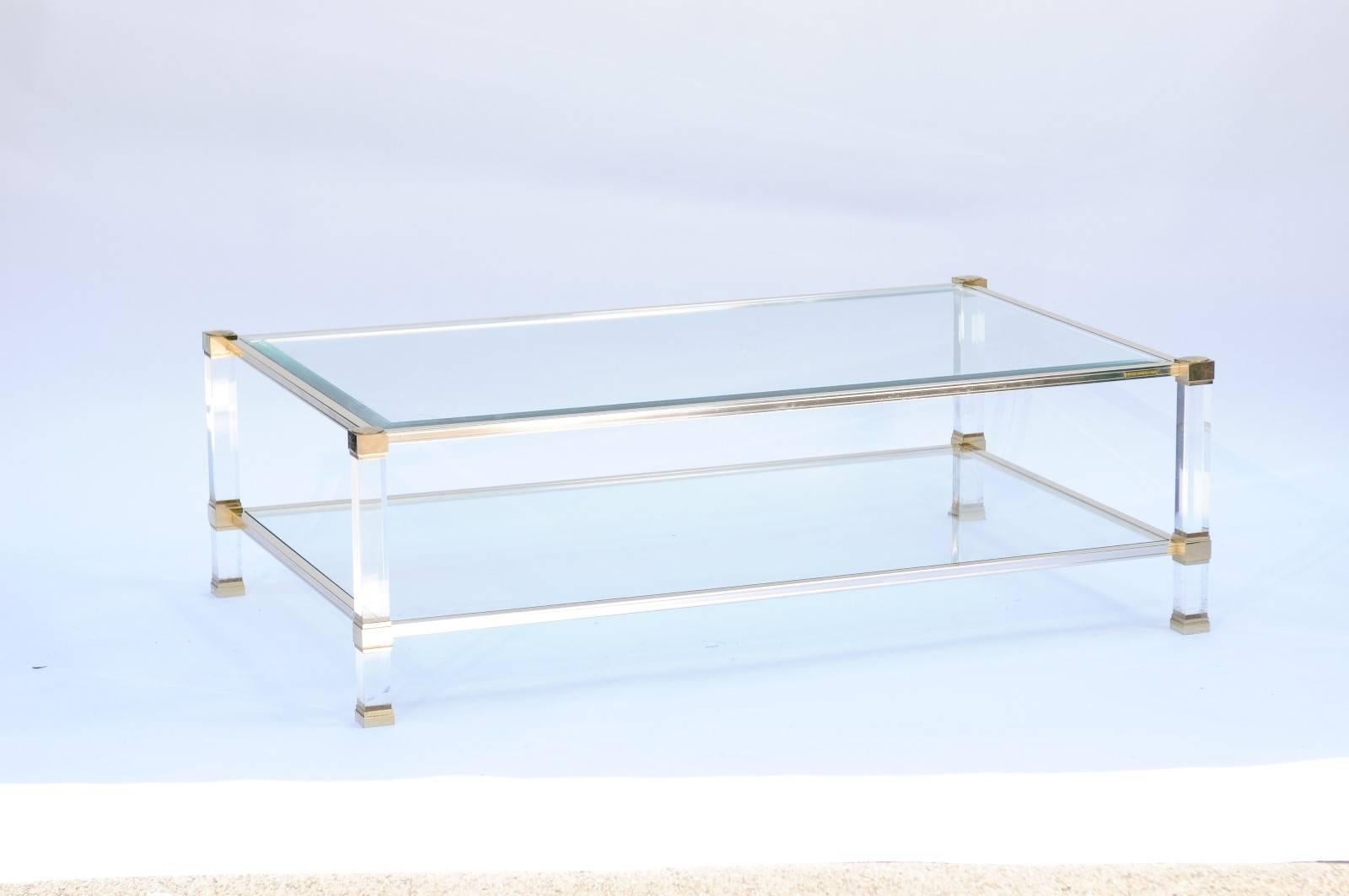 Cette table basse Pierre Vandel à deux niveaux, de style français moderne du milieu du siècle, présente un plateau rectangulaire en verre sur une étagère inférieure assortie, soutenue par une armature linéaire ornée d'accents dorés. Cette table