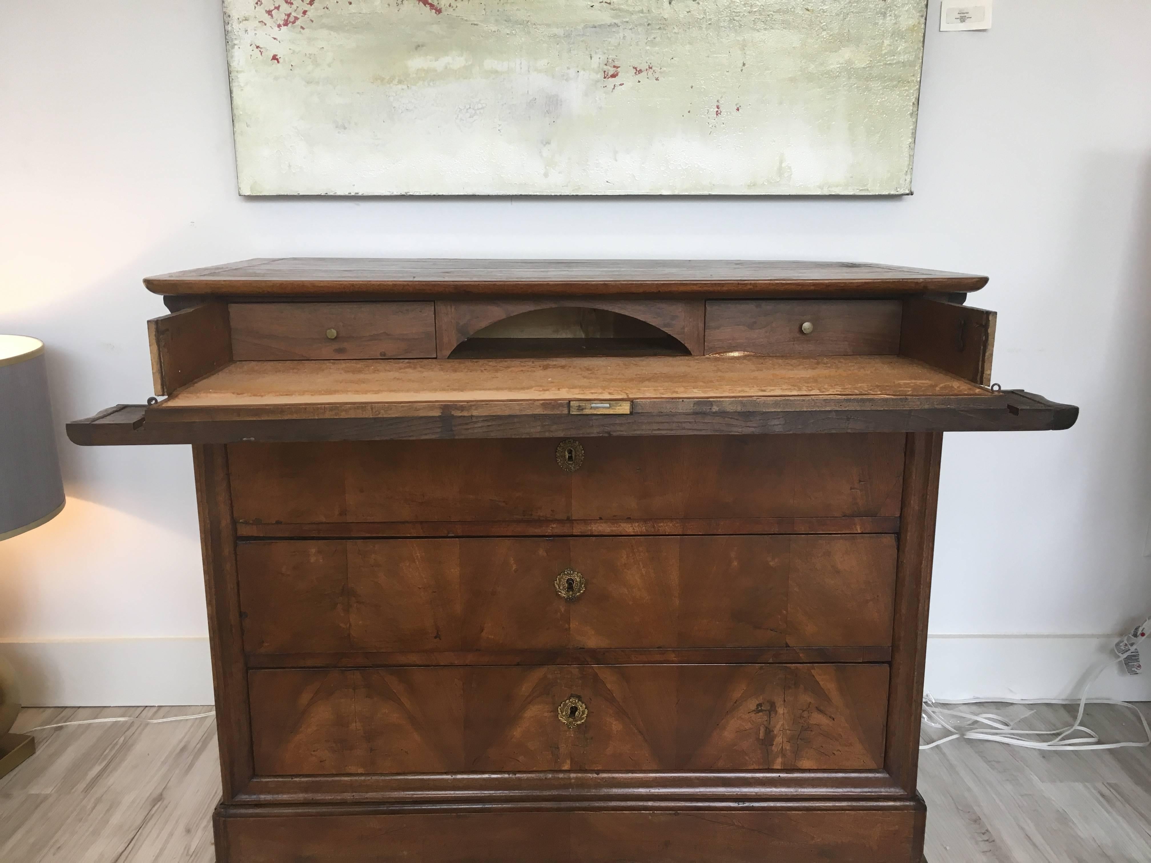 This French Louis Philippe style walnut commode features a rectangular top with rounded corners in the front over three deep drawers, topped by a pull-out desk section with drop-down front and a grey key frieze inside. The perfect combination of
