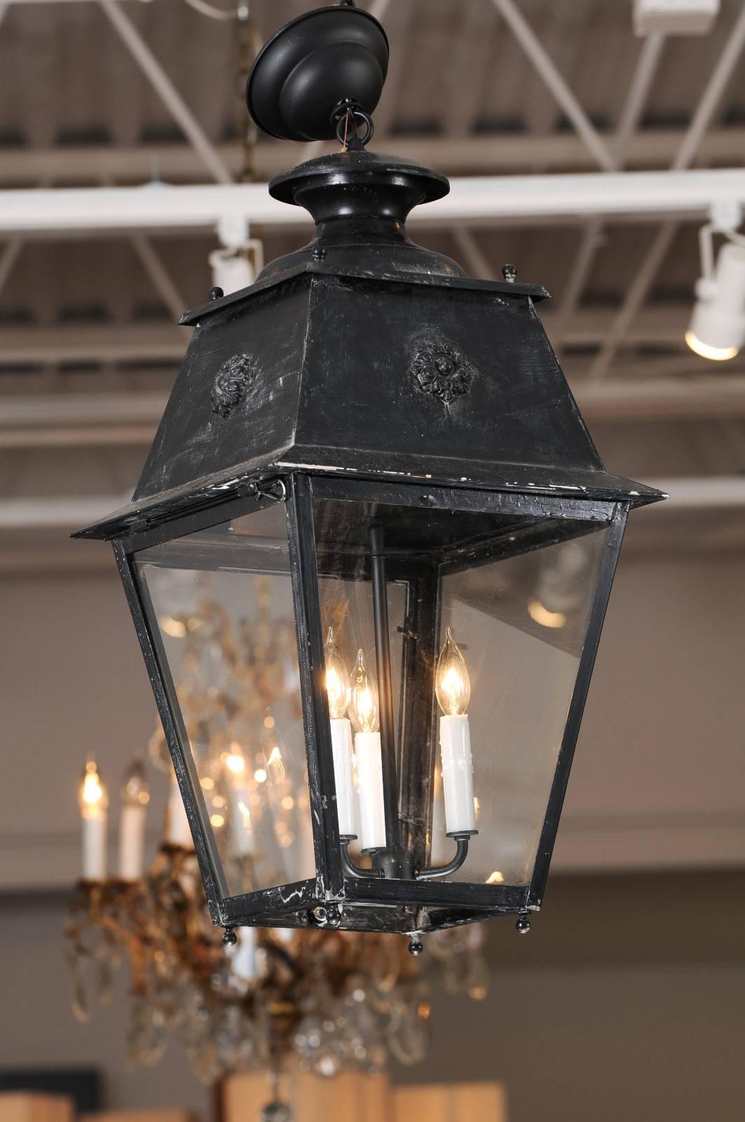 A pair of antique French black iron three-light lanterns from the late 19th century with rosette motifs and glass panels. From the south of France come these painted antique lanterns, both of which feature sleek, black metal framework, four sides of