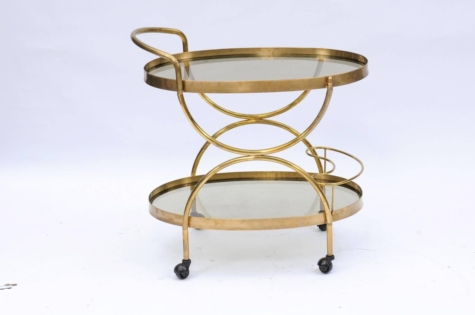 An Italian Mid-Century Modern oval two-tiered brass and glass bar cart with half-moon supports and smoky glass from 1950s, Florence. We are always looking for unusual bar carts that can double as consoles or gorgeous stand-alone bars, so when we