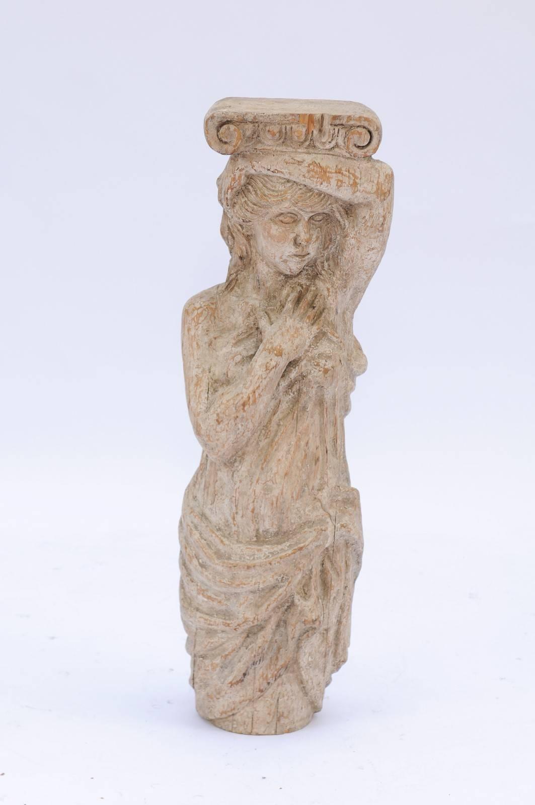 A French 18th century wooden carved statue of a woman. This French sculpture from the 18th century features a Greco-Roman lady elegantly raising her left arm above her head while her right hand is touching her hair. Her tunic drapes her Silhouette