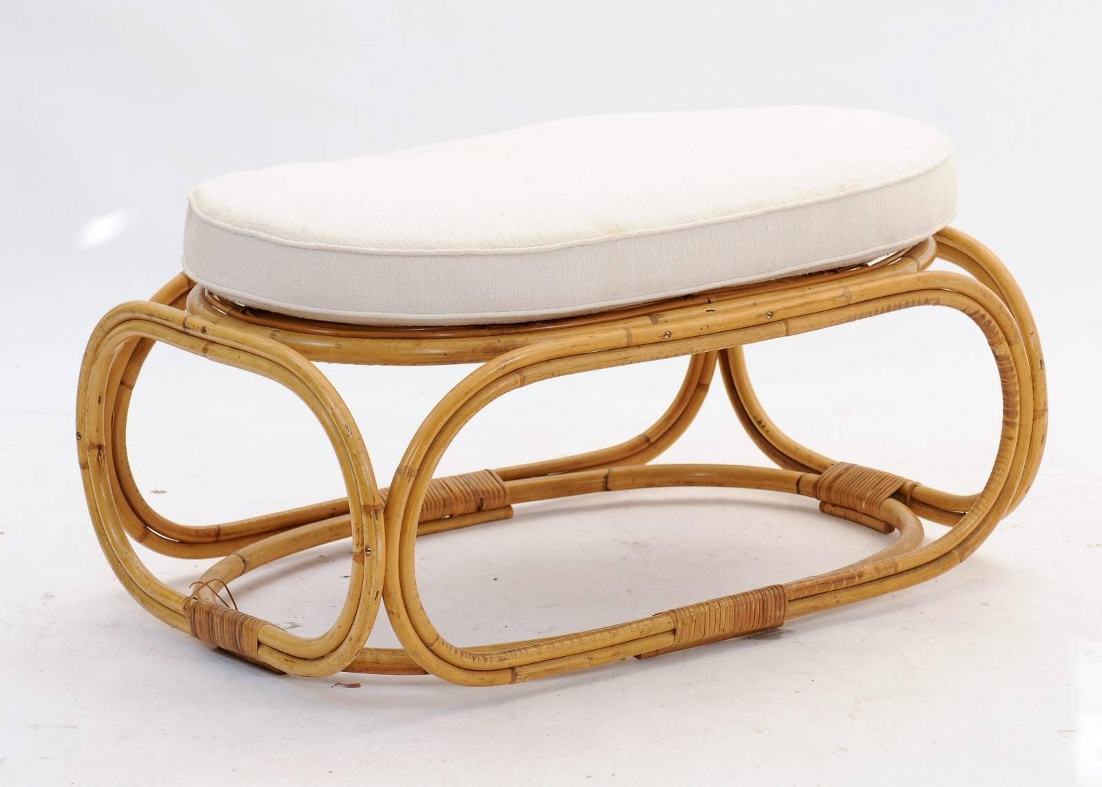 A French Mid-Century Modern rattan ottoman with rounded base and oval upholstered seat. Curvy and playful, this retro 1950s ottoman makes its mark by the pool or on the veranda. We love the rounded base and comfy seat and how the whole piece exudes