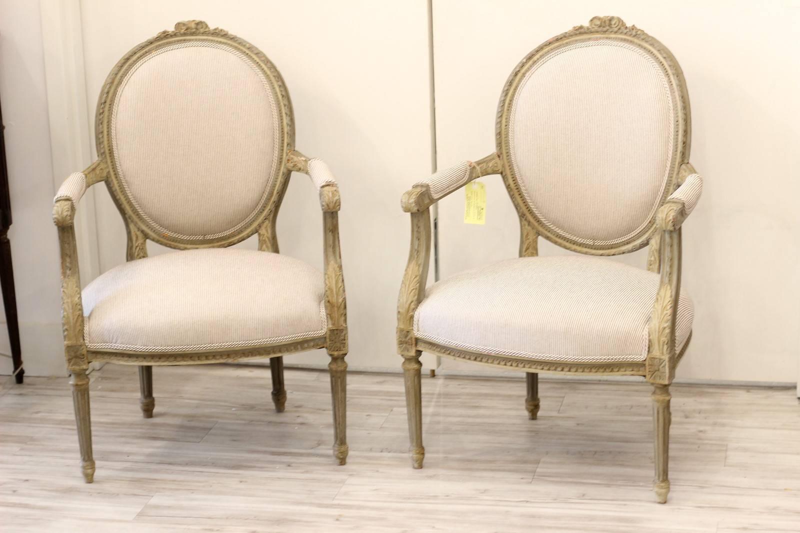 A pair of French oval back Louis XVI style carved and painted wooden armchairs from the late 19th century with striped cotton upholstery. The Louis were very comfy in these heavy, antique chairs featuring oval backs, carved crests on the top rails