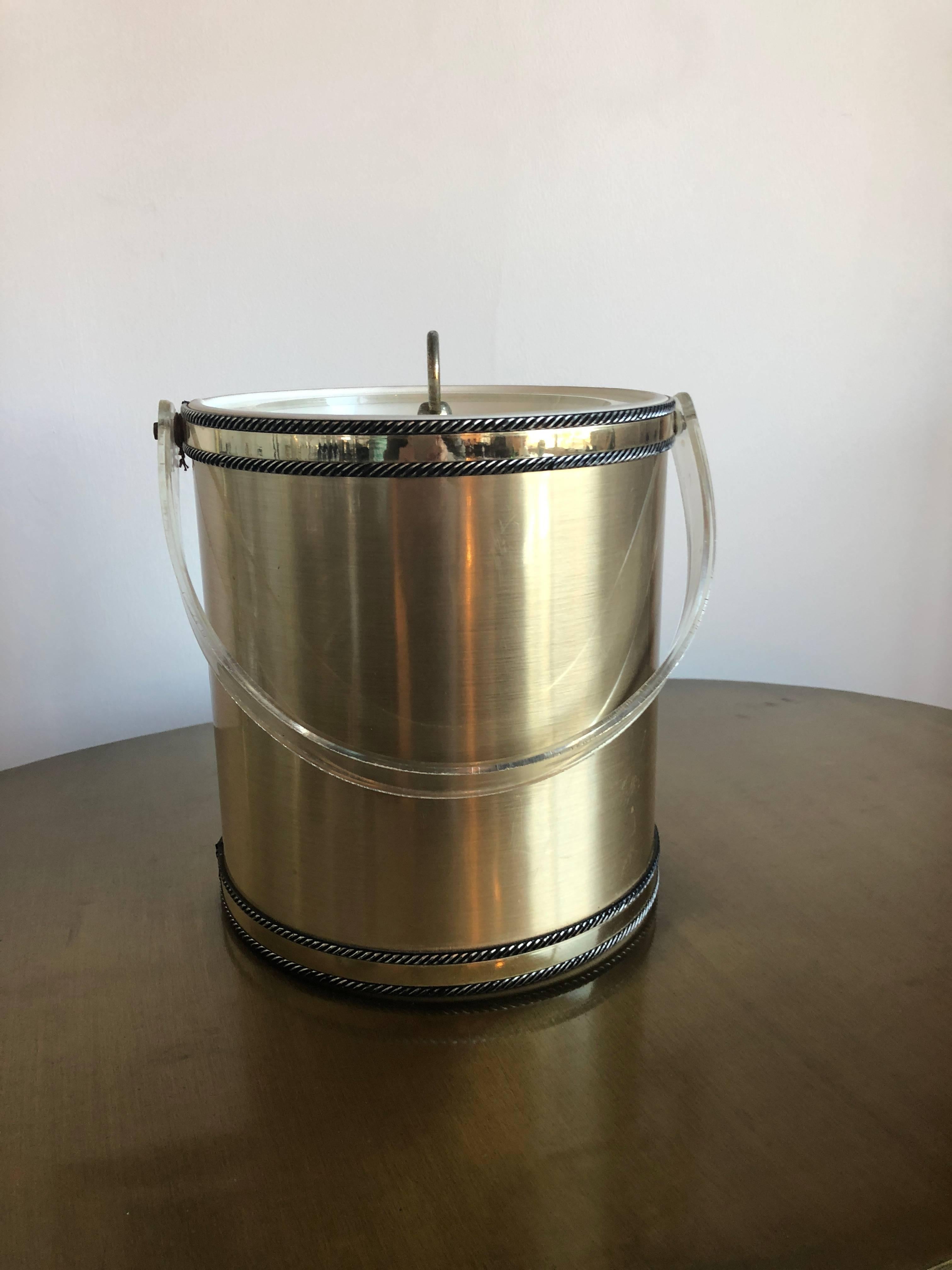 Offered is a signed Mid-Century Modern Georges Briard brushed brass and Lucite ice bucket. The brushed brass ice bucket has a cylindrical shape with bands of polished brass at the top and bottom bordered by applied roping with a clear Lucite swing