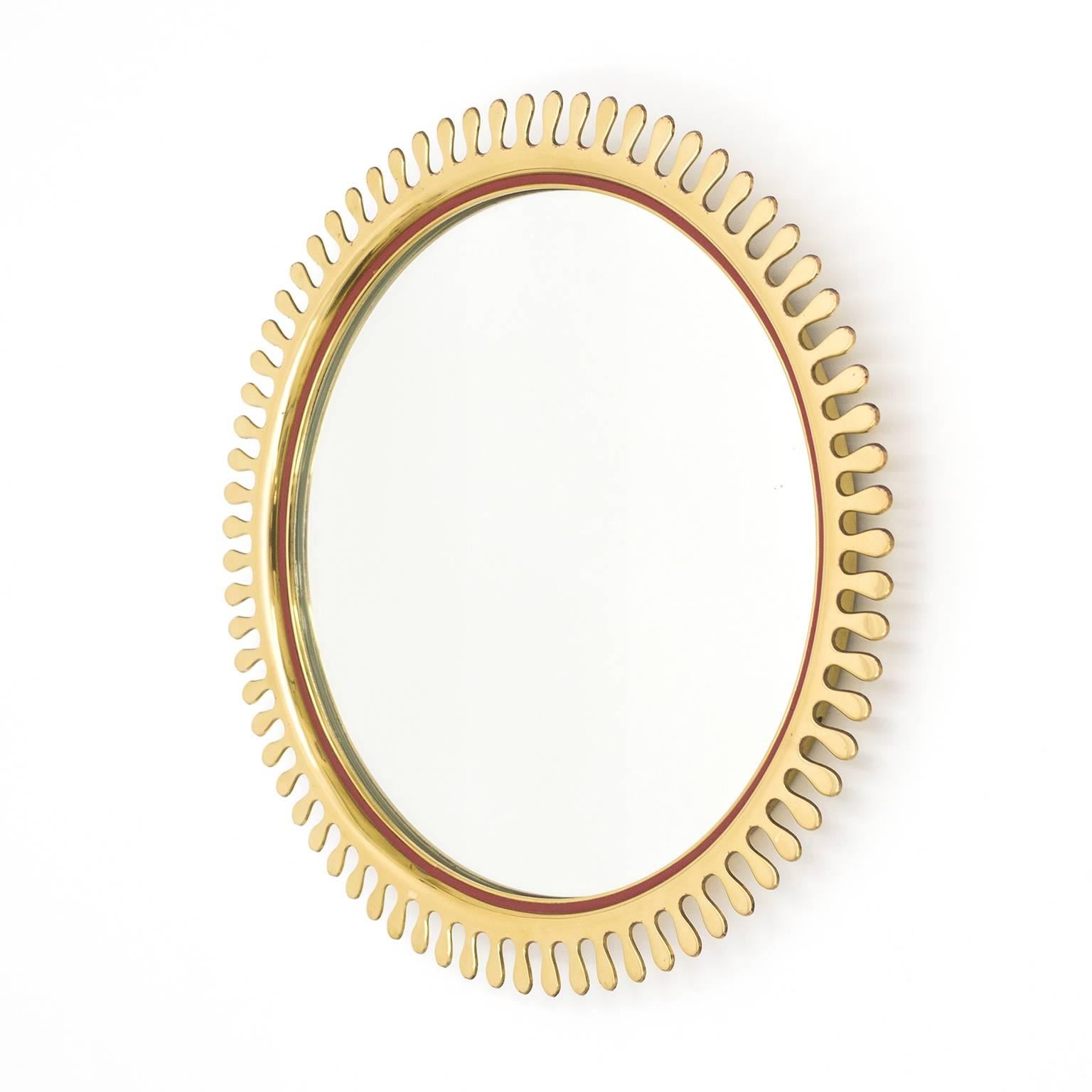 Beautifully crafted Mid-Century brass sun mirror. Made of thick, solid brass this represents a very unique take on the sunburst motif. Along the inside of the rim is a slim bordeaux colored leather or faux-leather band. Beautiful original condition
