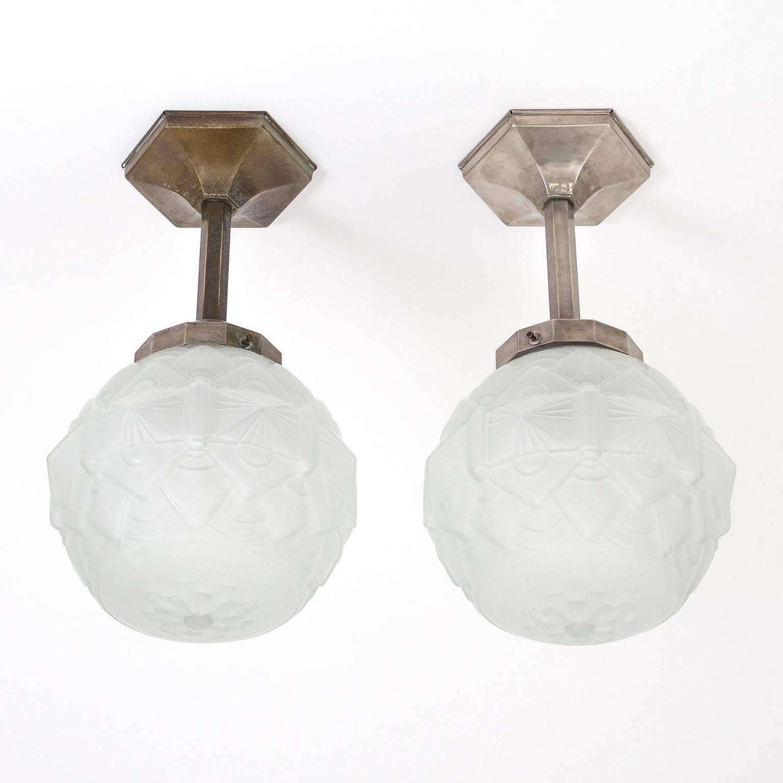 Elegant pair of French Art Deco ceiling lights with nickeled brass hardware and satin textured glass globes. The hardware has a very geometric design with a hexagonal canopy and stem and becoming more intricate in the globe holder. The acid