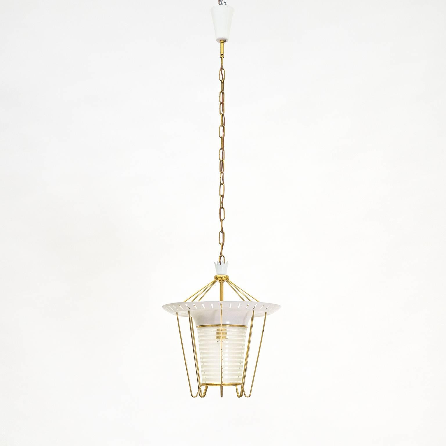 Delightful italian pendant or lantern from the 1950s with a modernist touch. White lacquered aluminum, delicate brass elements and glass with frosted stripes give this an airy mid century elegance. A charming patina on the brass and some light loss