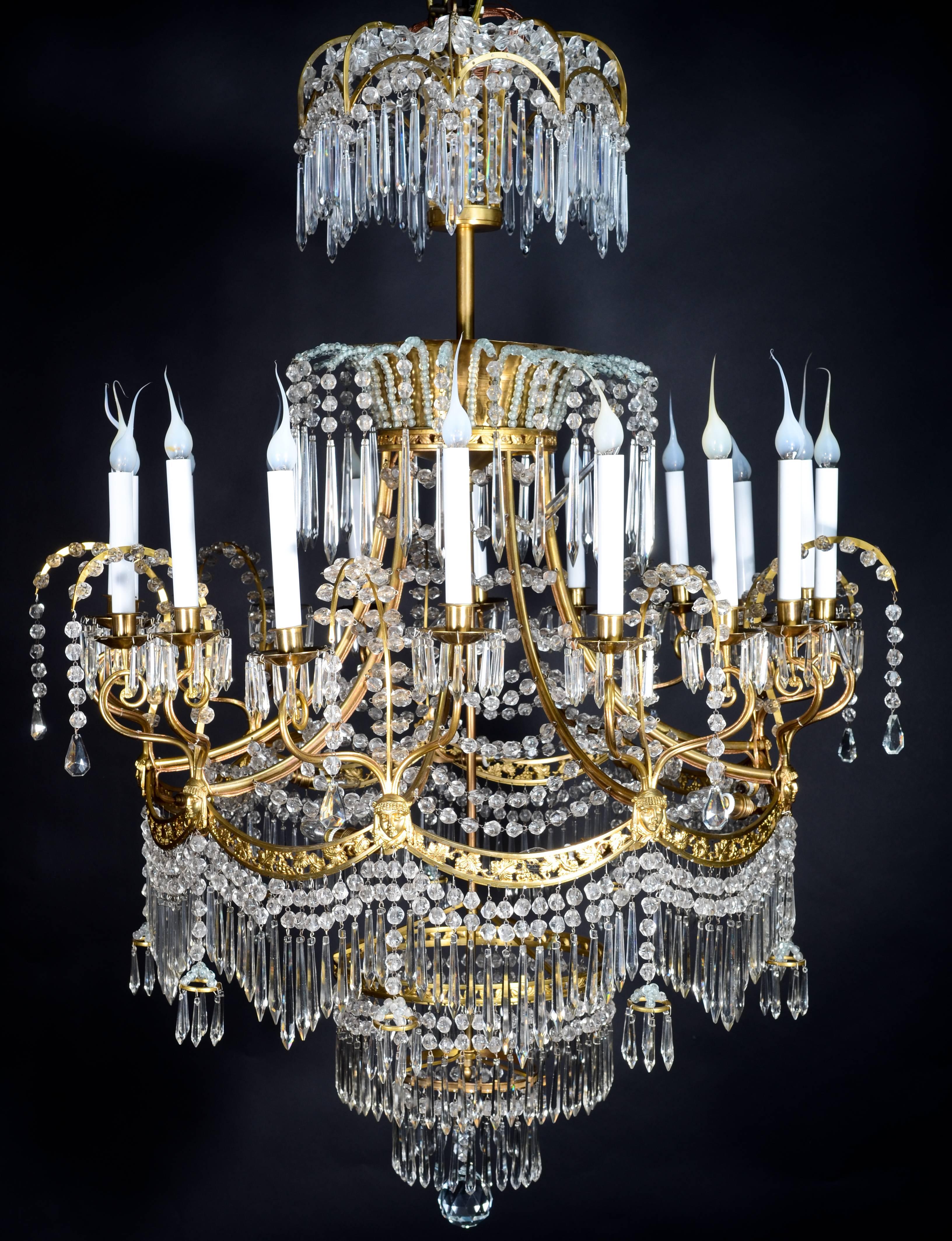 A palatial and large antique Russian neoclassical gilt bronze and cut crystal multi light chandelier of fine detail embellished with figural masks, cut crystal prisms and cut crystal chains.