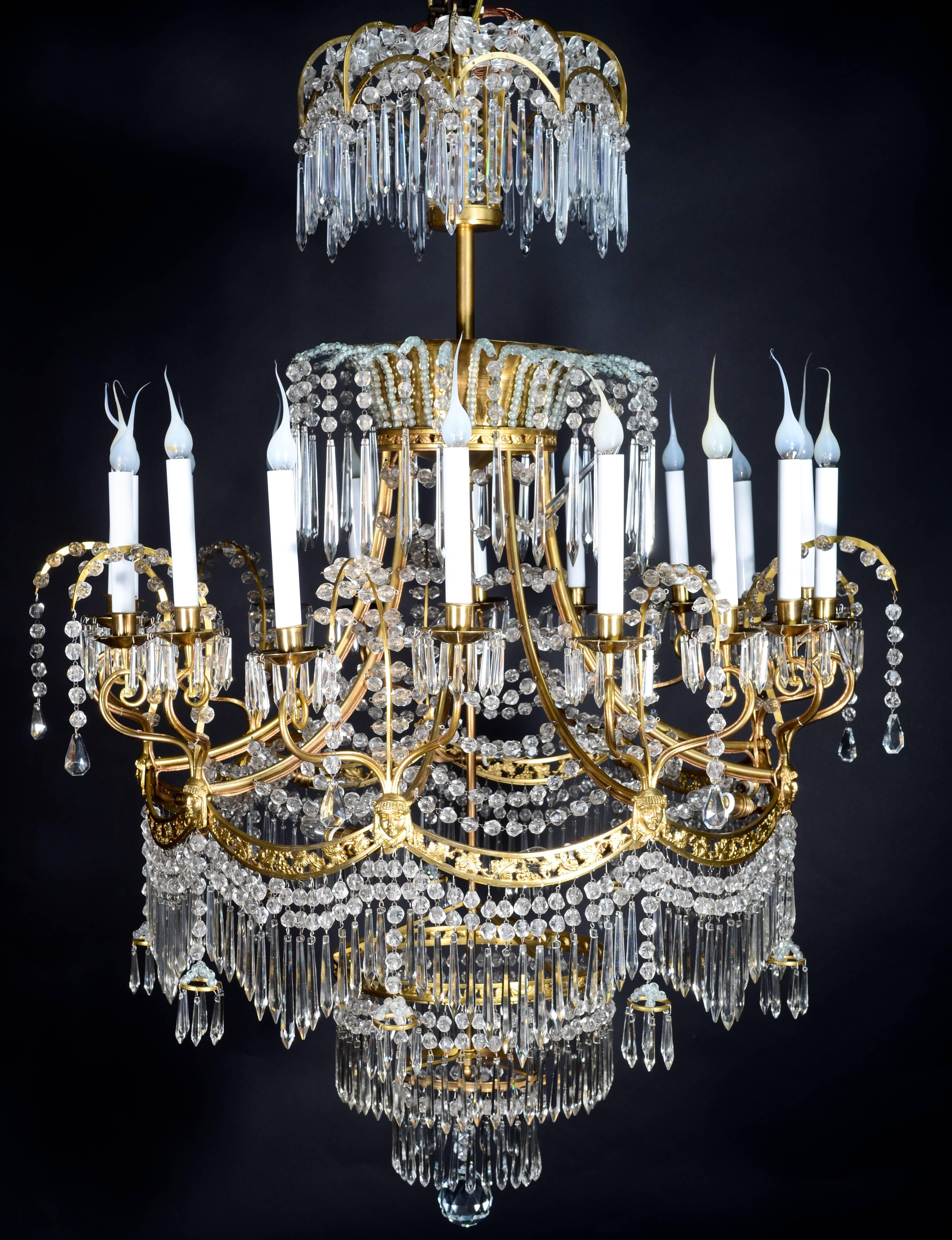 Un grande lampadario antico russo neoclassico in bronzo dorato e cristallo tagliato dai dettagli raffinati, impreziosito da maschere figurative, prismi in cristallo tagliato e catene in cristallo tagliato.