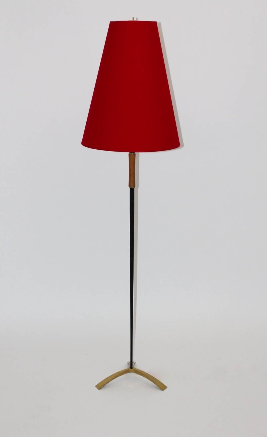 Mid Century Modern red black metal tripod floor Lamp by J. T. Kalmar, 1950s Vienna, Austria.
The floor lamp shows a brass tripod lamp base with a  conical metal stand black lacquered and a wooden handle.
One socket E 27, renewed red fabric shade