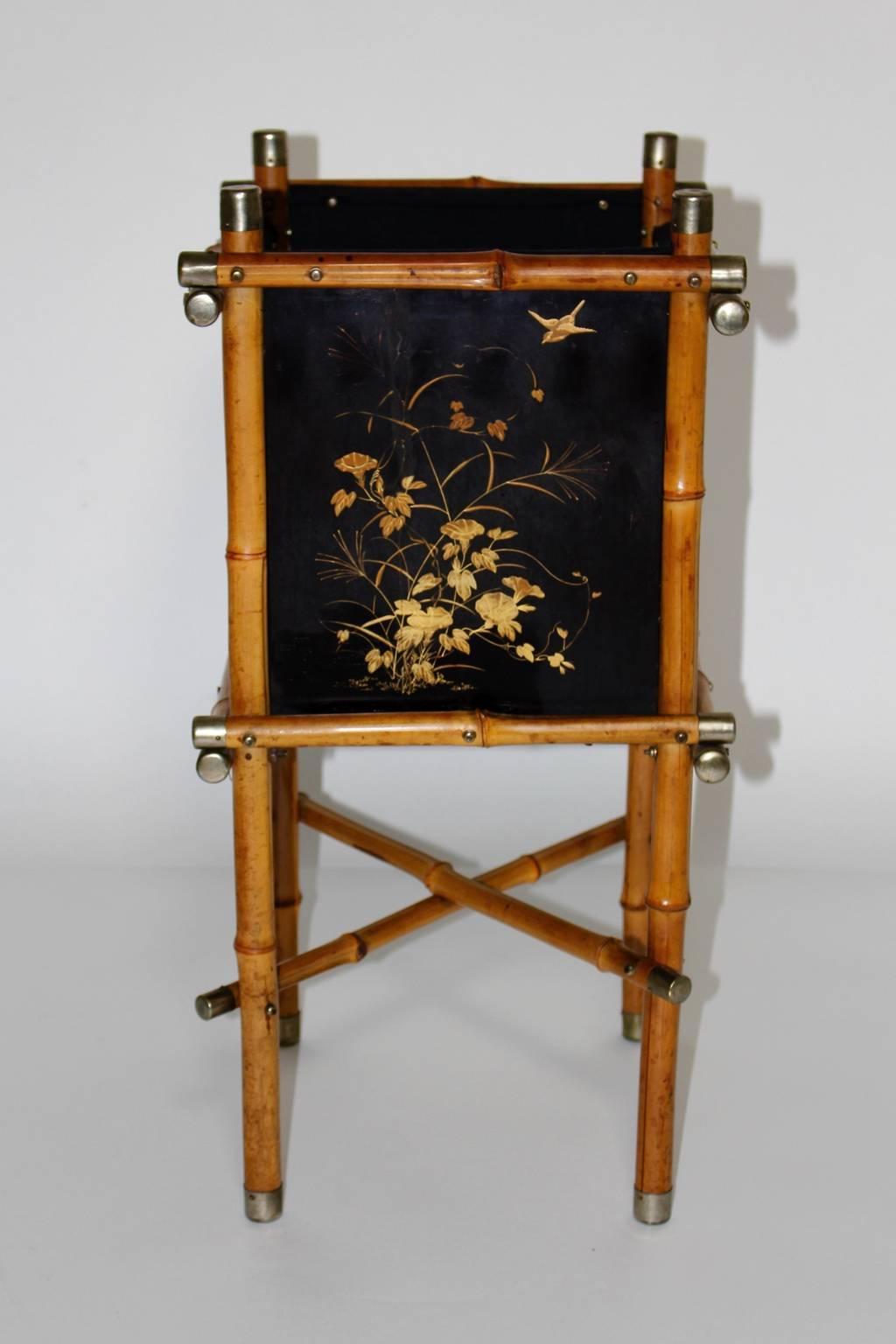 An elegant Art Deco vintage bamboo flower stand or paper basket, which features bamboo sticks. The fittings of the sticks are nickel-plated. 
The side parts are made of black plywood with golden hand-painted delicate flowers and birds and