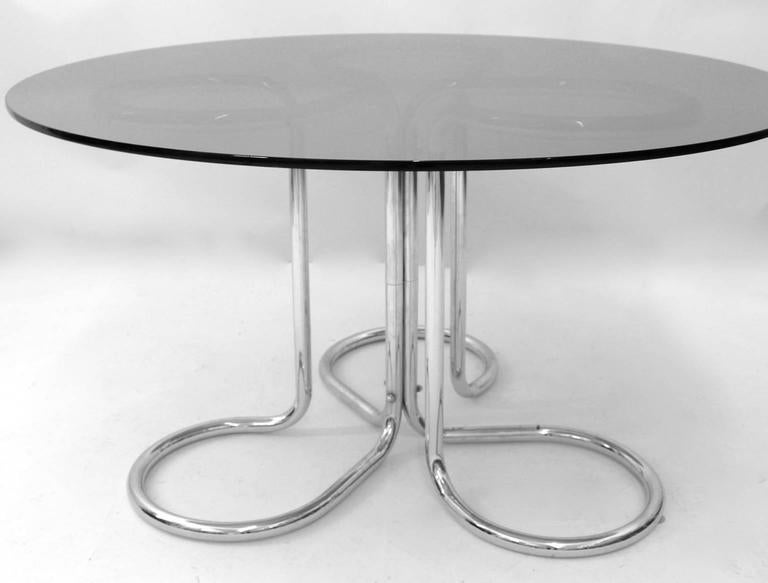 A space age vintage dining table by Giotto Stoppino 1970s Italy, which features a curved chromed steel tube base construction. The dining table is topped with a round smoked glass top.
The original condition is very good with signs of age and