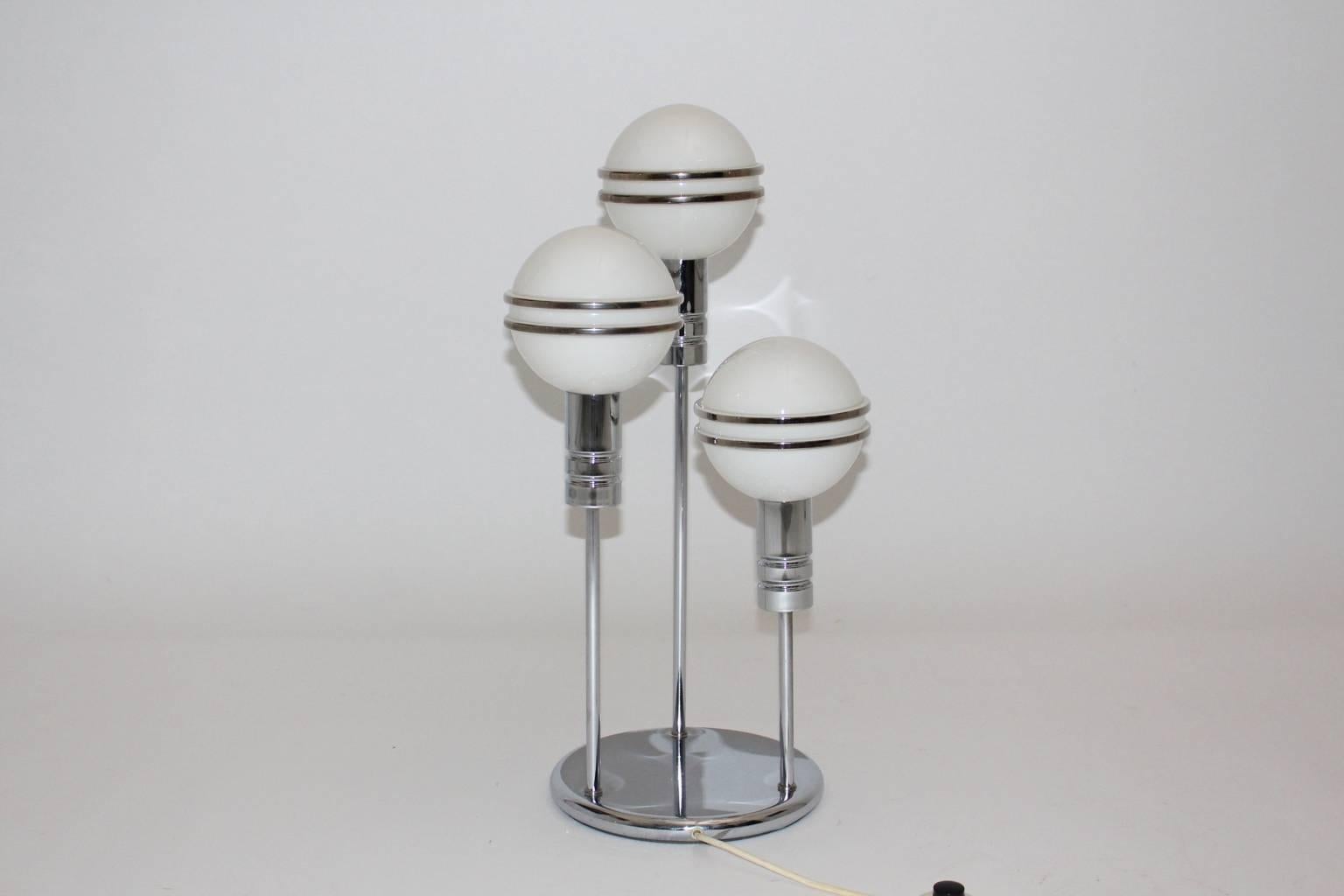 The streamline Art Deco Era table lamp is made of chrome-plated steel with three white milk-glass globes.
Each globe is decorated with linings.

The table lamp lights with three bulbs E 14 and has an on/off switch.
The table lamp is in very good