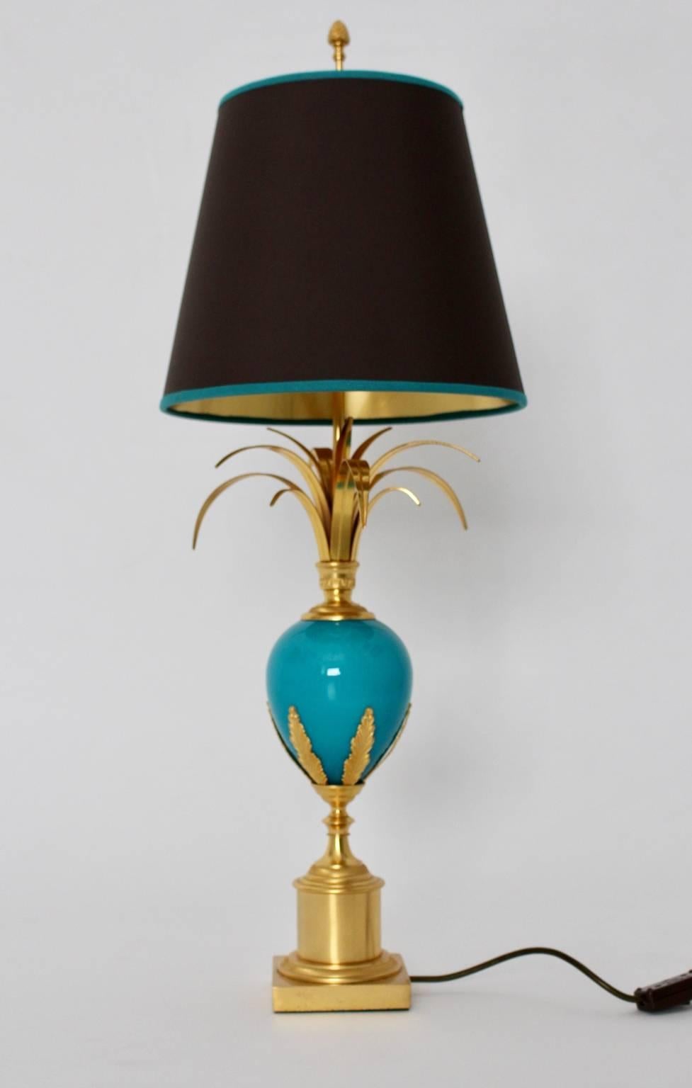 The table lamp in the style of Maison Charles was designed and manufactured circa 1970 in France.

The materials of the base are brass gilded and a turquoise glass egg decorated with brass gilded ornaments and stylized palm leaves.
The renewed