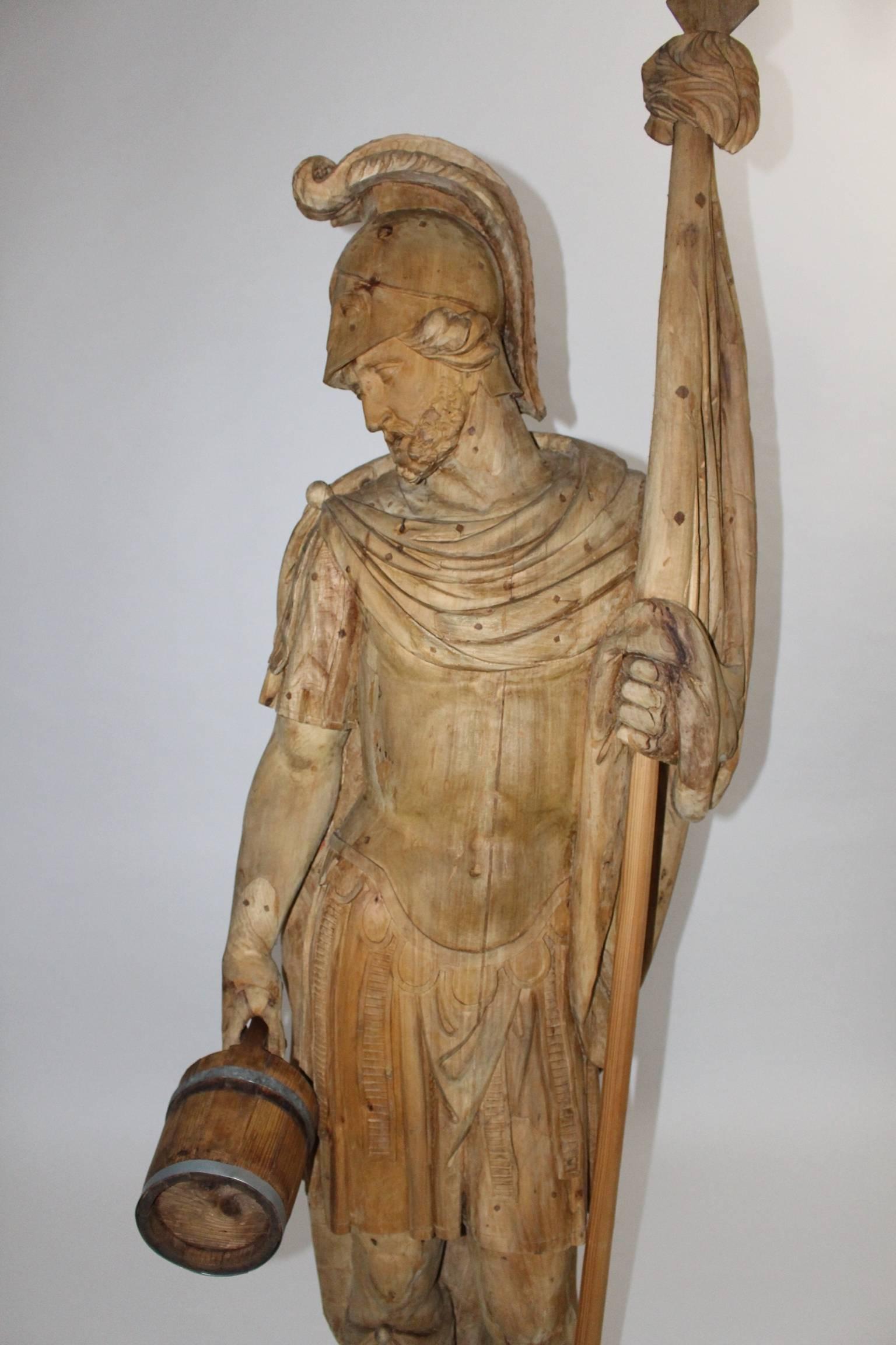 This huge hand-carved figure shows the protector and patron against fire, Saint Florian.
St. Florian is dressed like a roman soldier and his attribute is a water bucket.
The figure was made of hand-carved basswood, spruce and metal rings, which are