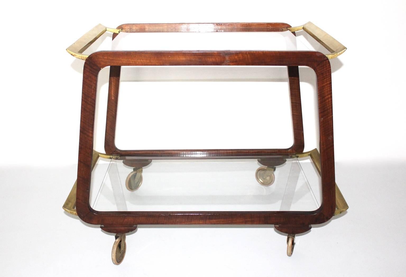 Mid Century Modern beautiful bar cart or serving trolley  designed and executed in Vienna in the 1960s. While the walnut frame and a brass reling refinish the look, two clear glass tiers gives the cart elegance.
Very good vintage condition with