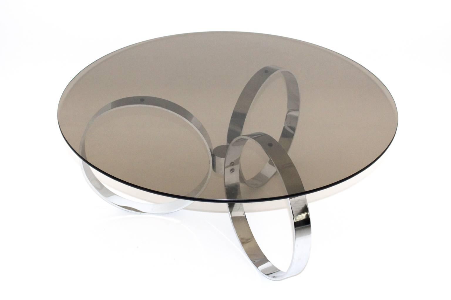 This coffee table has a base with three solid metal chromed rings. Also the top features a smoked clear glass plate.

The measures are:
Table base diameter 70 cm, height: 41 cm
Table with the glass top diameter 99 cm, height 42 cm.
all measures are