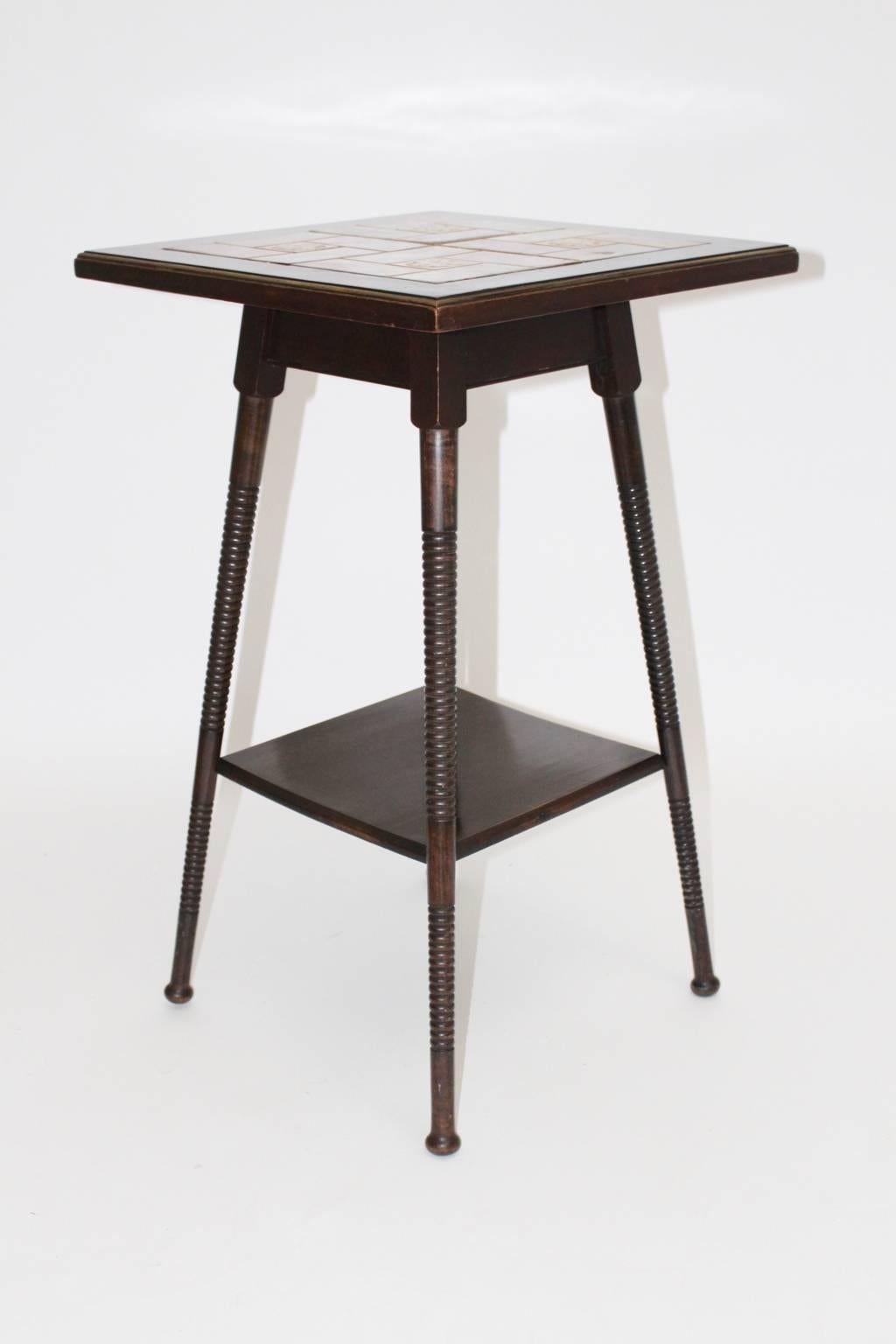 Two-tiered side table, beechwood brown stained with turned legs.
The top shows the original green and redbrown ceramic tiles and a brass edge.
This kind of side table was used by Adolf Loos for his apartment.

Literature: Adolf Loos; Burkhard