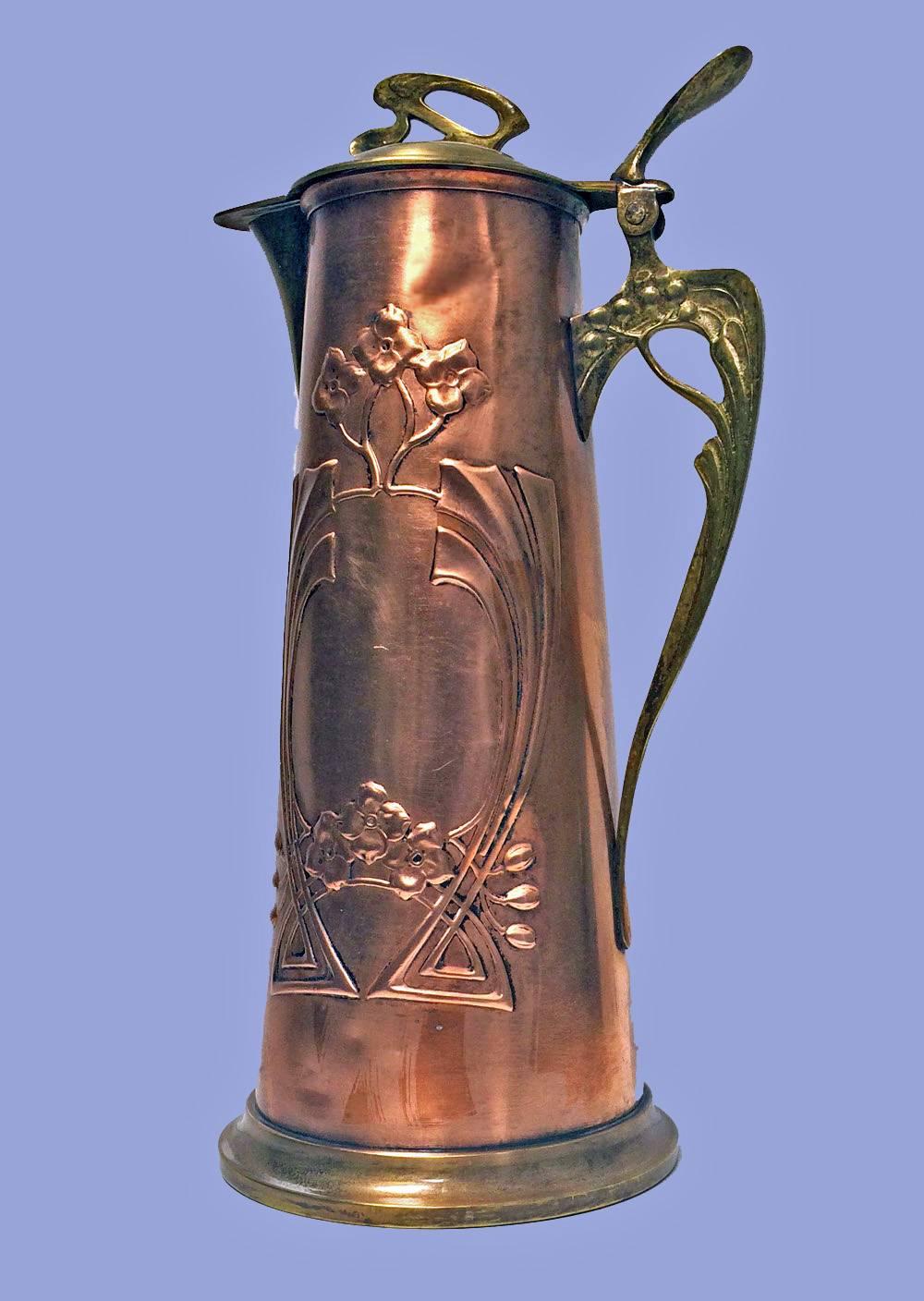 Arts & Crafts copper and brass pitcher jug, probably, Germany, circa 1900. The slightly tapered jug decorated with motifs in celtic manner and stylized handle and thumb piece, plain moulded base, hinged dome shaped cover, stylised thumbpiece. Marked