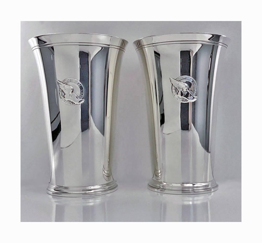A pair of Tiffany & Co, New York athletic club sterling silver mint julip cups with applied club insignia and engraved on base 'Trapshooting‘ 1937 and 1938 respectively. Each of tapered plain flared form, lightly gilded interiors. Height: