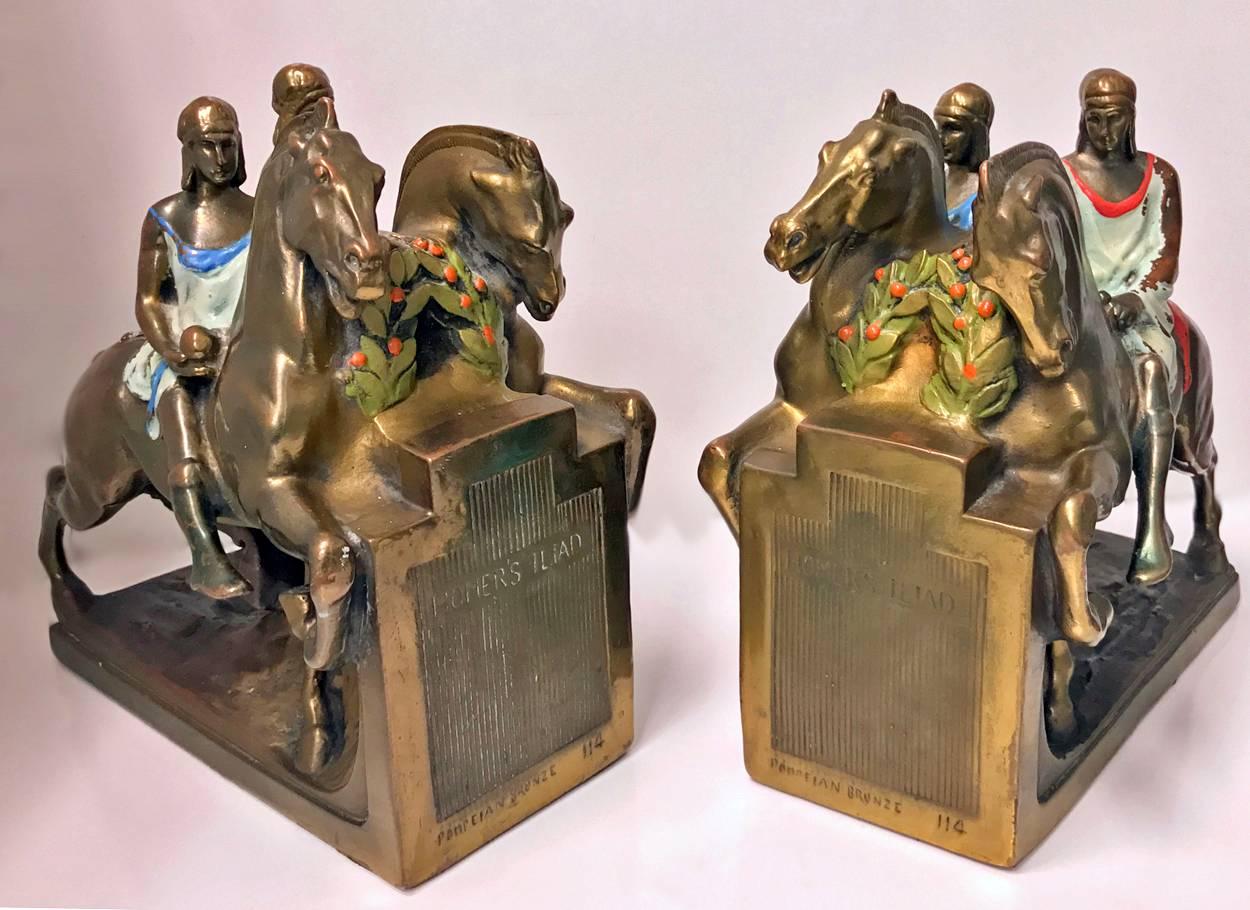 Large pair of bronze clad bookends by Pompeian Bronze, circa 1920s. Each depiocting two men on horseback from Homer's epic Iliad. Polychrome paint decoration. Some paint loss commensurate with age, otherwise in very good condition. Each measure: 9