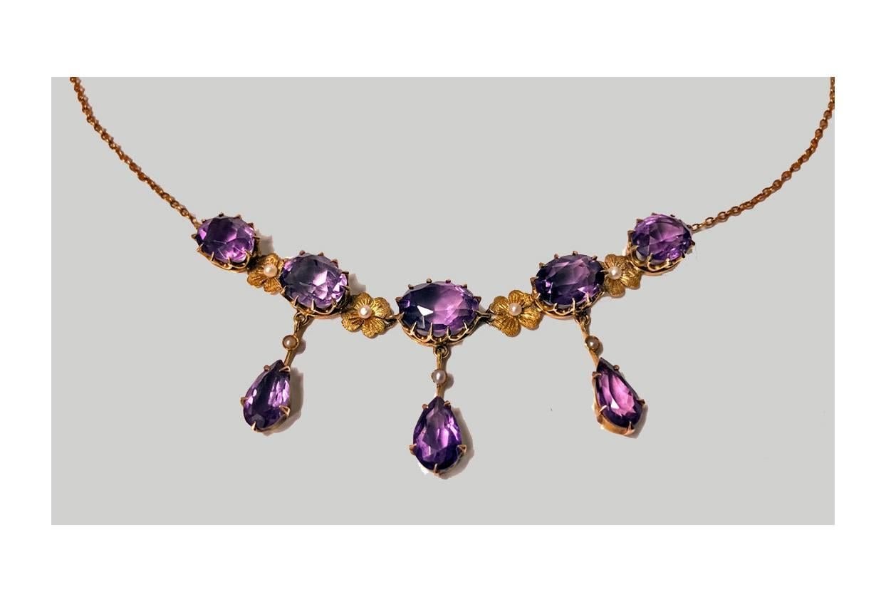 Early 20th century 14 karat amethyst and pearl lavalier necklace, American, circa 1910. The necklace claw set with five oval faceted medium tone amethyst, inter spaced with gold floral seed pearl rosettes, three amethyst suspending tear drop