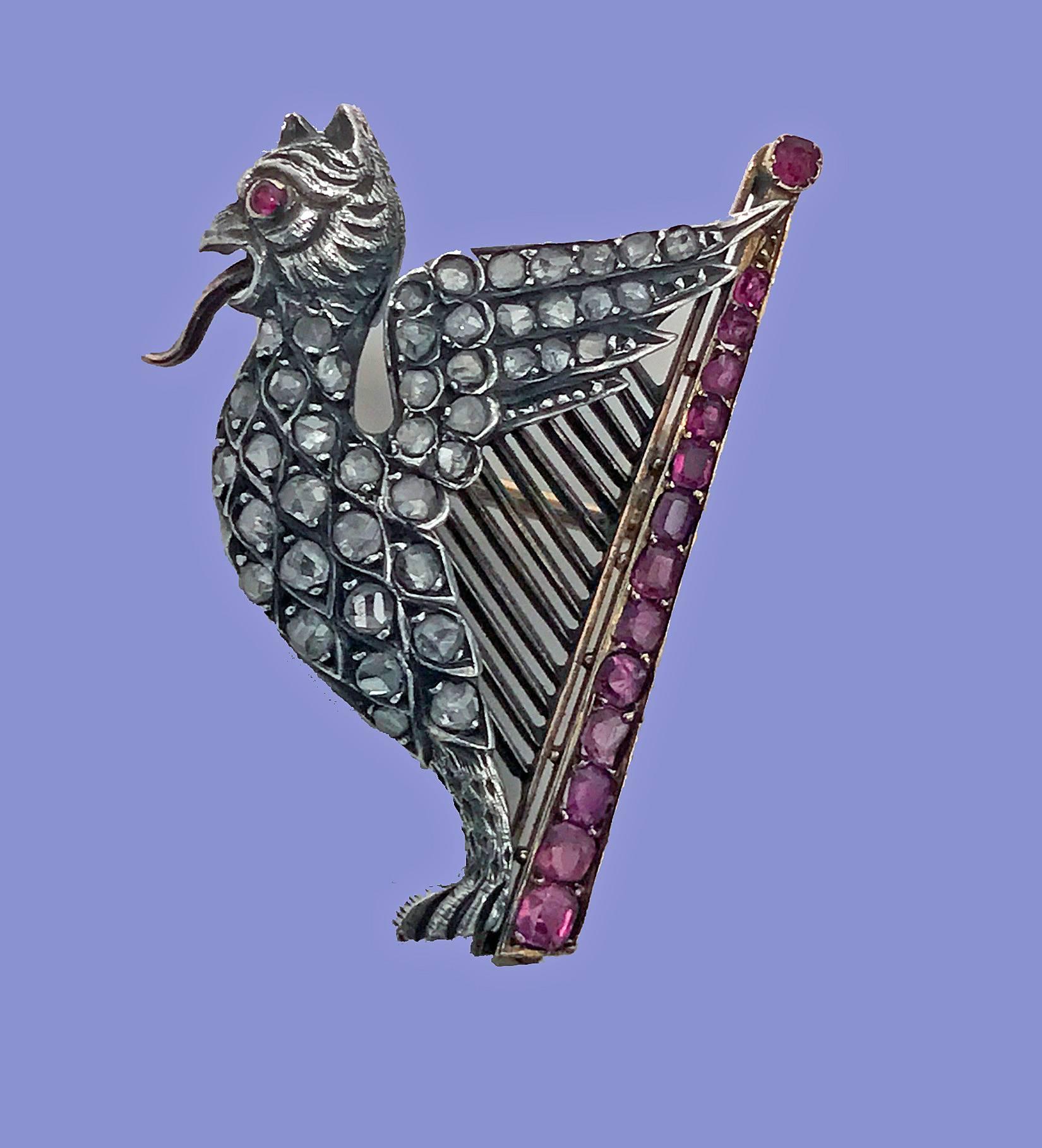 French Griffin and Harp ruby, diamond, pearl and 18-karat (tested) brooch, circa 1890. The winged griffin and harp brooch set in silver and gold. The tongue protruding griffin set with 43 small rose cut diamonds and cabochon ruby eye, realistic