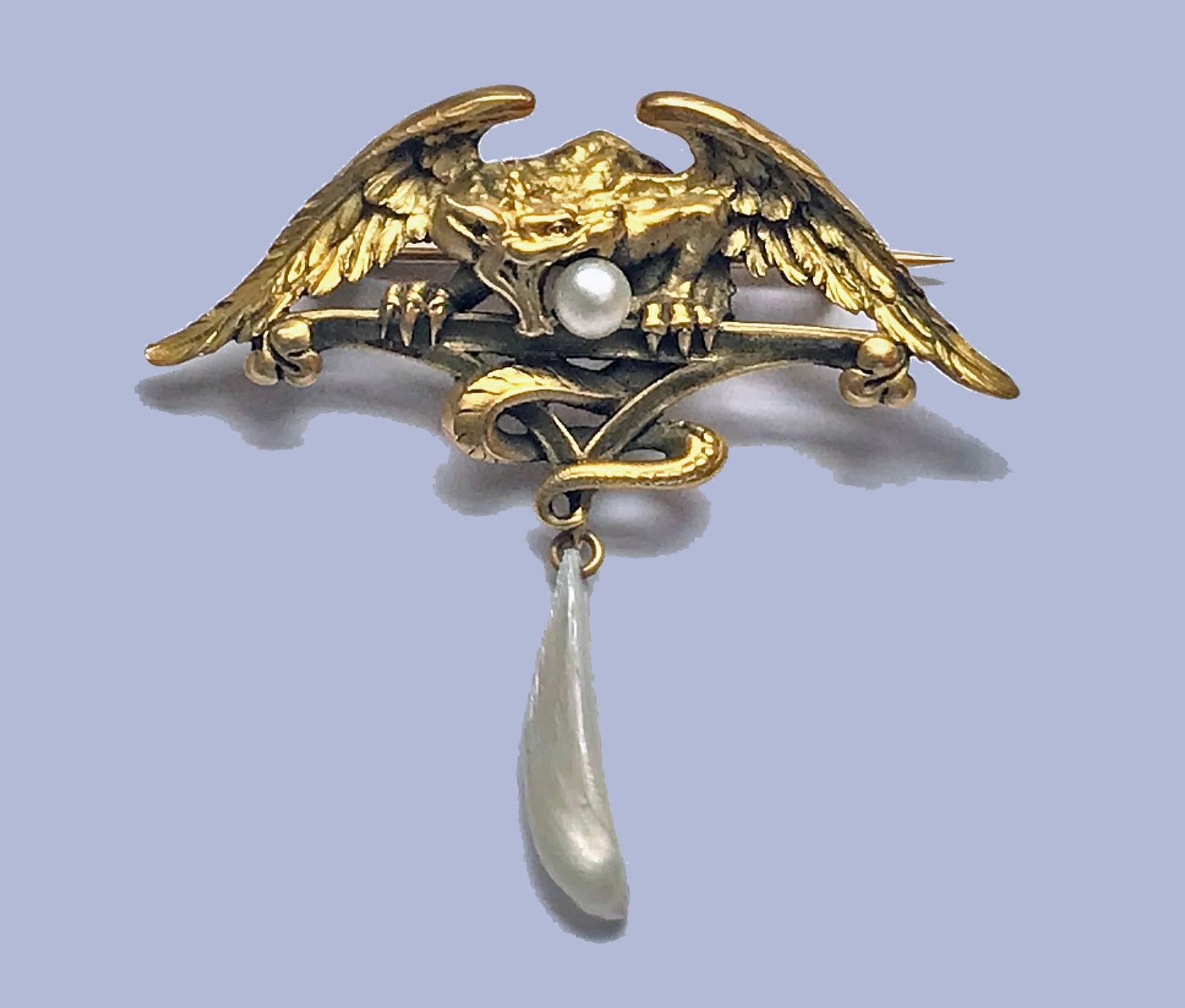 French Art Nouveau 18K mythological brooch Pendant, C.1900; depicting a mythological combination including part eagle, part serpent griffin carrying a pearl in mouth and suspending a mother of pearl. Width (wing spread): 2.25 inches. Drop: 2 inches.