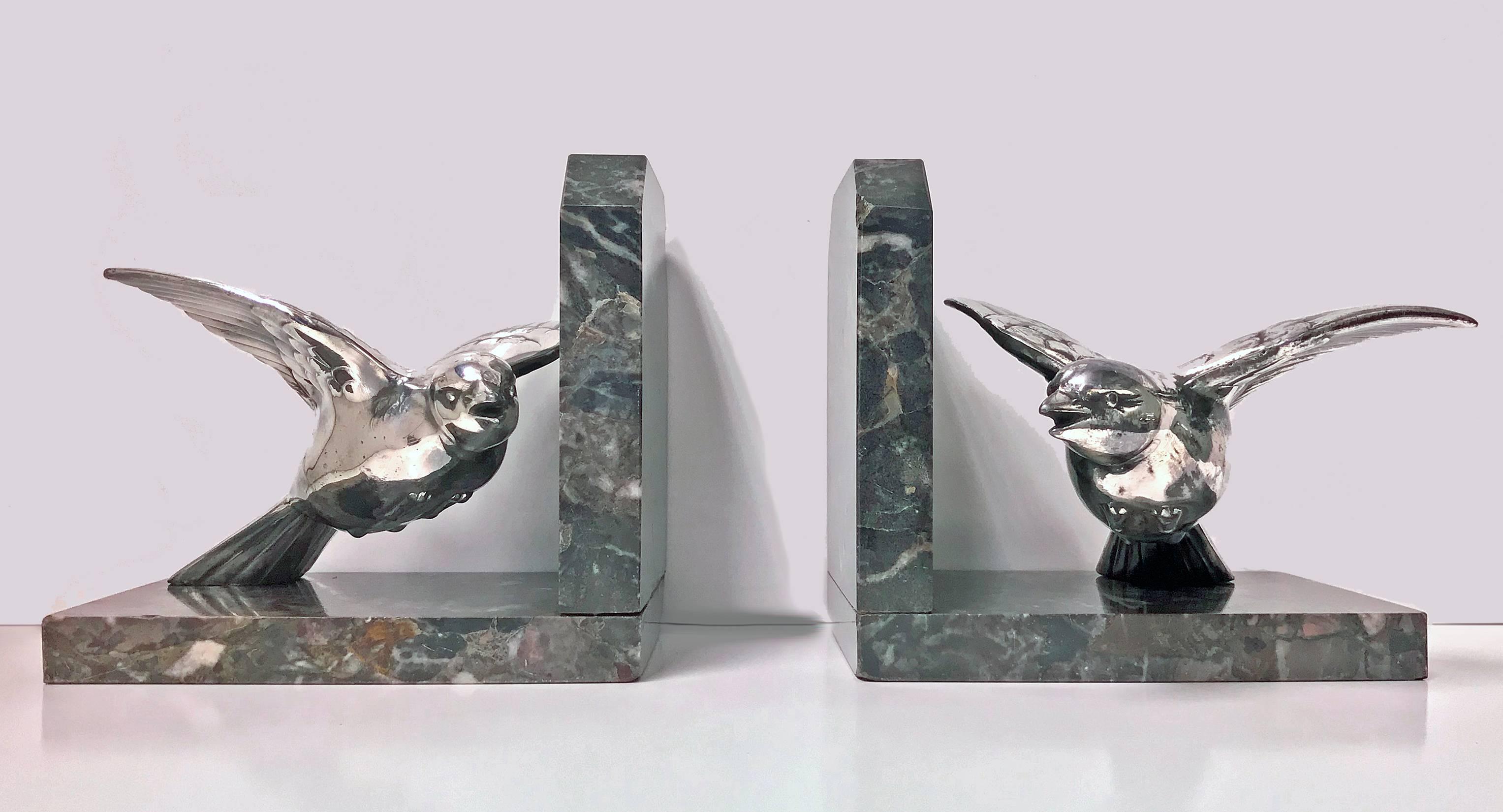 Pair of Art Deco white metal bookends in the form of flying birds, probably France, circa 1930. Each depicting a bird on marble base. Each of realistic model form textured body; surmounted on mottled grey brown and white overtone marble base.