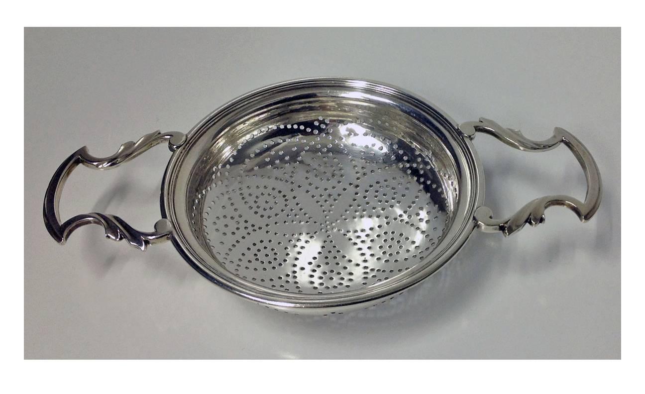 George 111 Silver Strainer, London 1774, William Plummer. The strainer of usual form, pierced bowl, foliate shaped handles, engraved with the crest of an oak tree fructed and penetrated transversely by a frame saw and motto above `Through’ – crest
