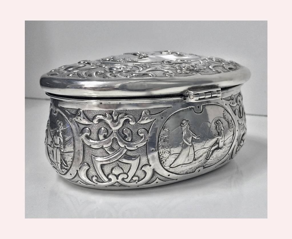 Large 19th century Hanau Silver box, C.1900. Each side of oval shape box with romantic figural scene. The hinged cover with figures playing musical instruments. Measures 5 x 3 3/4" x 2 3/4", Item weight 228.67 grams.