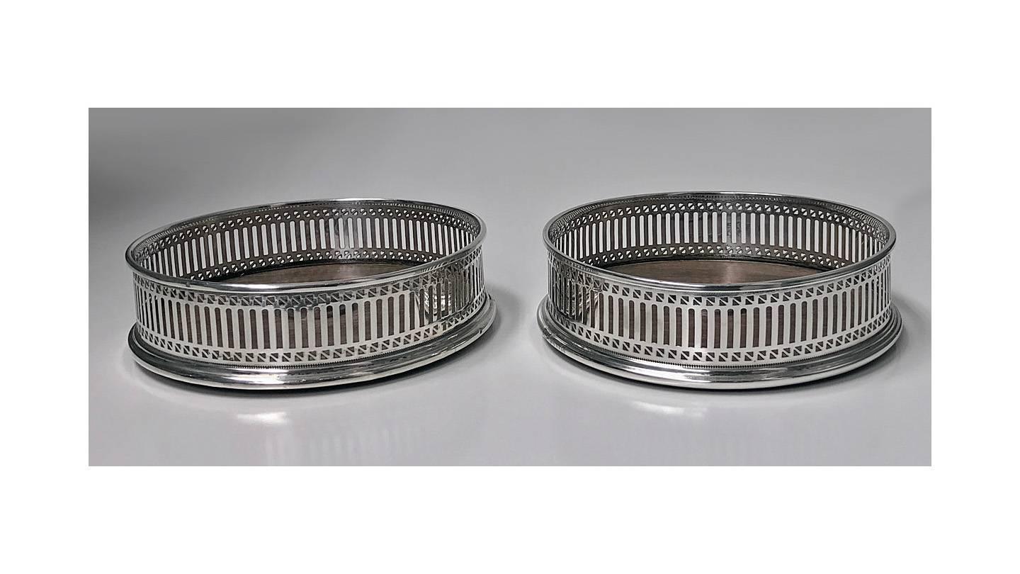 Pair of Georgian style English silver wine coasters, London 1975, A. Chick. The coasters of 18th century Georgian style, pierced geometric body design with upper and lower ovolo borders, turned wood bases. Measures: Diameter 5 inches., height 1.50