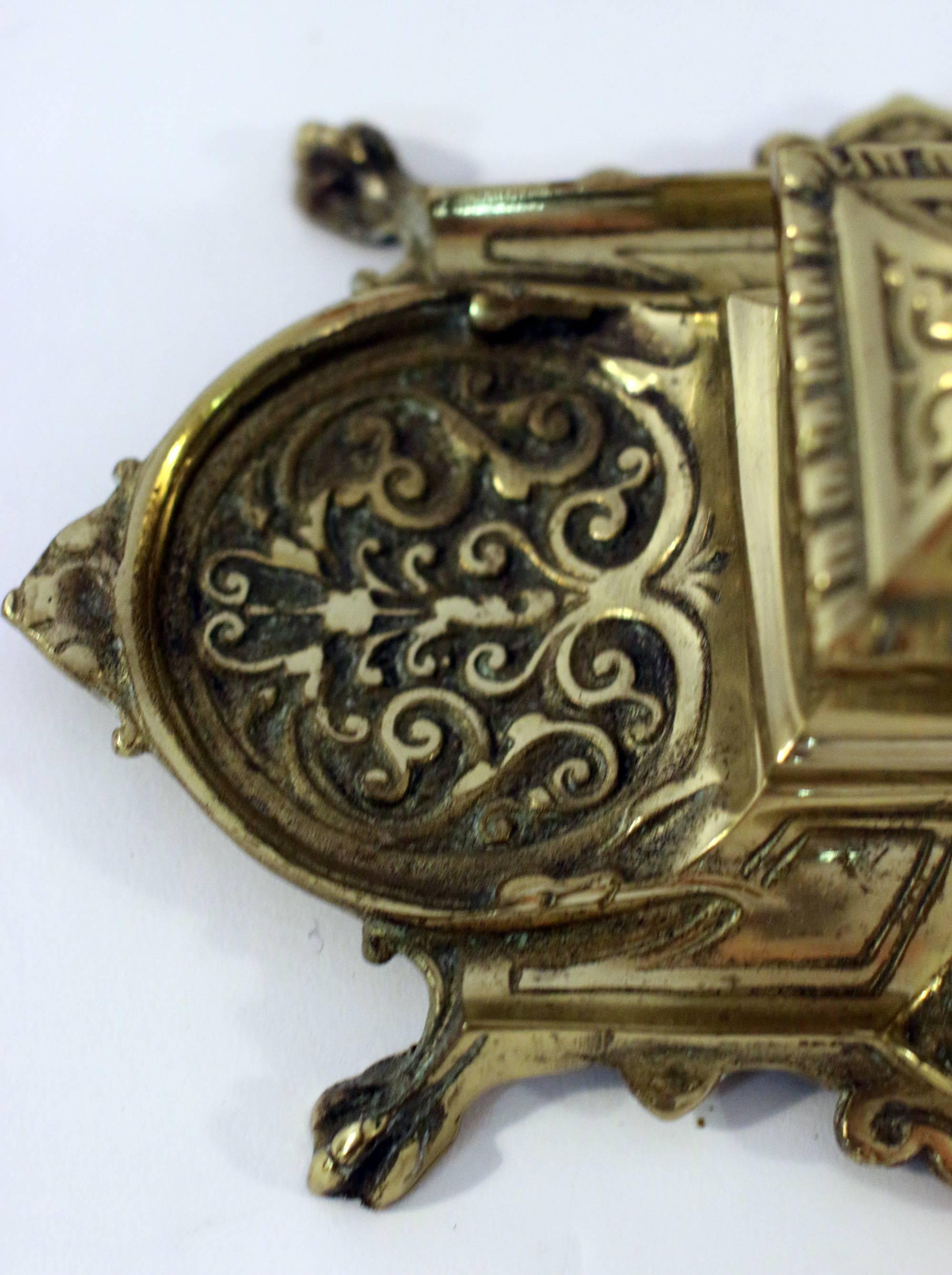 Petite size scrolled repousse brass single inkwell with lid. Features include an intricate design, paw feet and a glass well liner. Excellent condition with hinged lid intact.