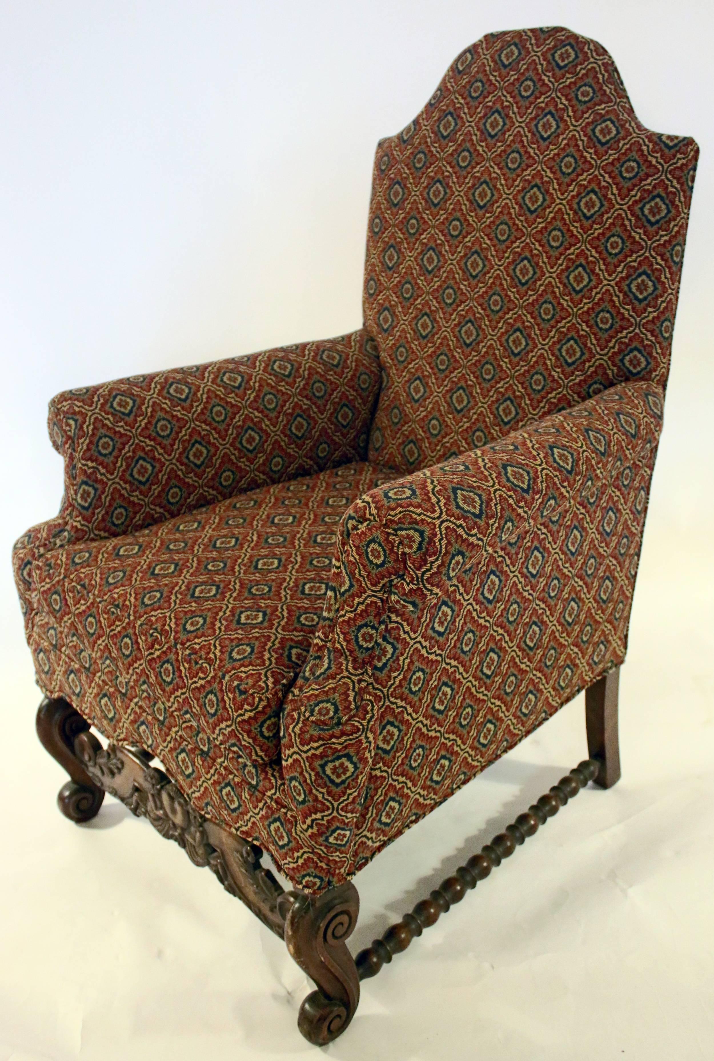 Pair of upholstered armchairs in the Jacobean revival style, circa 1890s. Features include a slight domed back and flared arms. Constructed on very sturdy frames of English walnut, the front bases are carved in a heart shape with a cherub on either