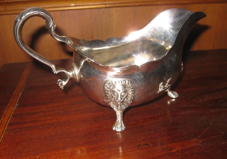 Irish sterling silver sauce boat featuring lion heads tapering into paw feet, a scalloped edge, a graceful handle. Marked with the symbol of Ireland and the harp fineness symbol. The makers first initial is J but the other initial is undetermined.