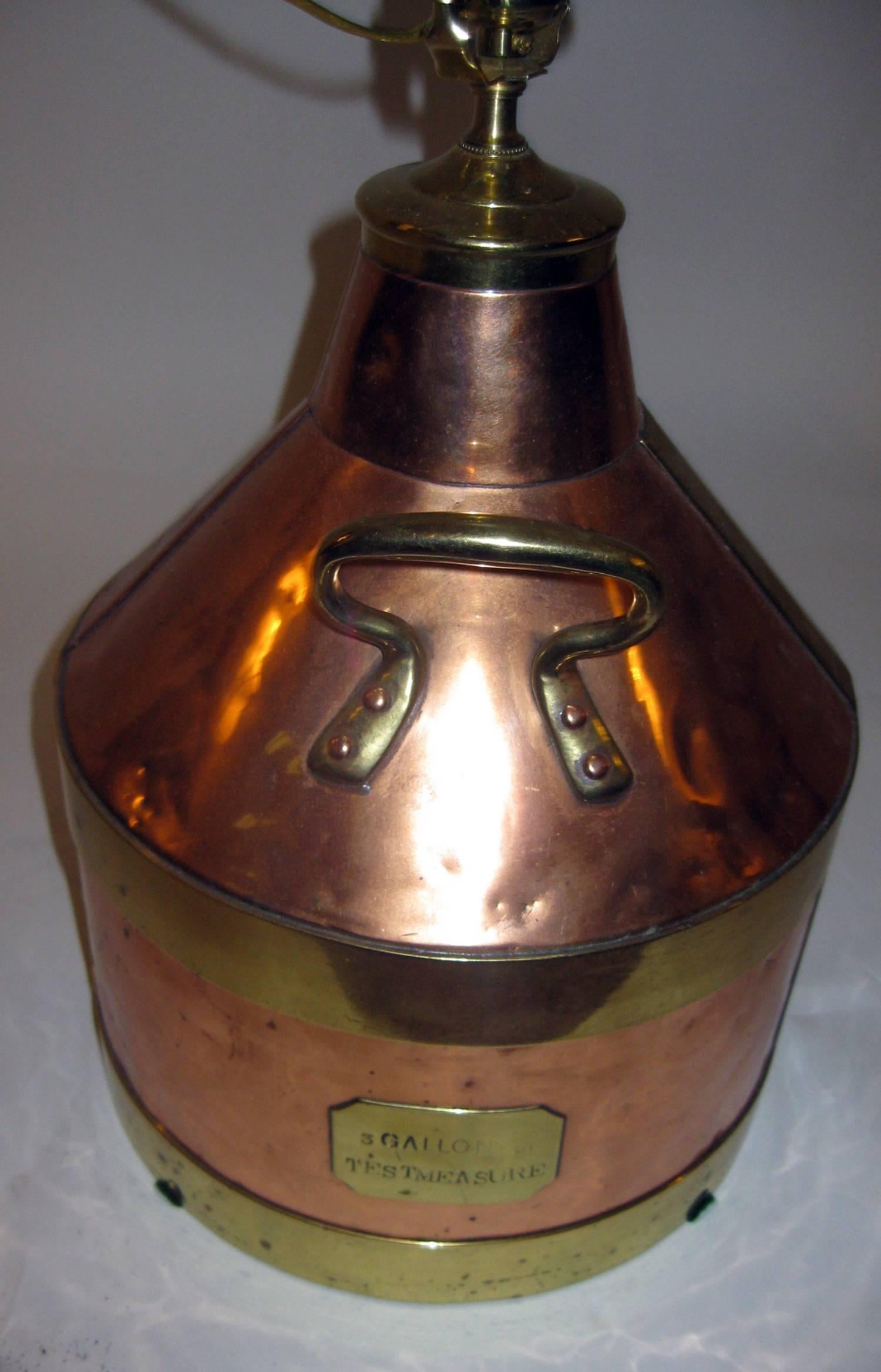 Table lamp converted from a large English copper jug. Features include applied brass riveted bales and handles with an appropriate burlap shade. In working condition, the jug itself has great patina and much character. There is an applied plaque