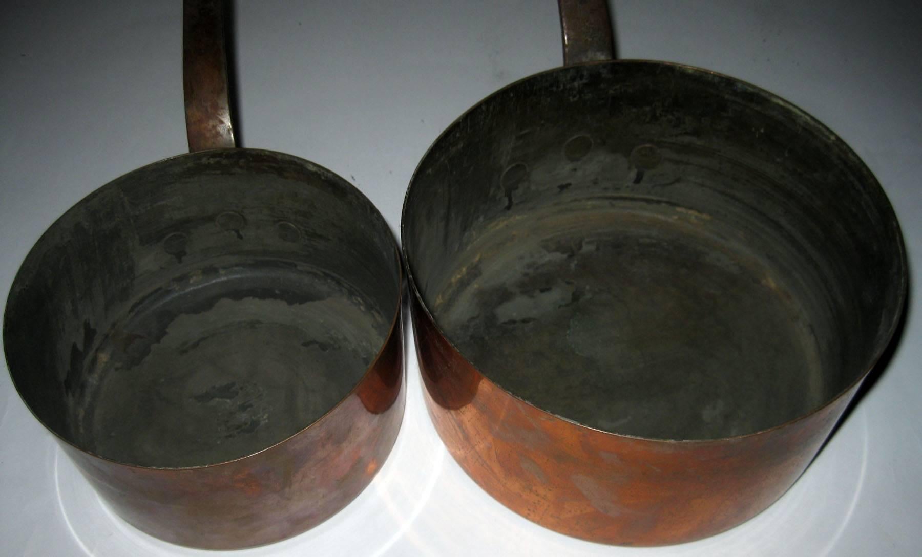 Pair of French copper sauce pans in graduated sizes featuring riveted metal handles with a slight tilt. Measure/ Large: 7.25 inches tall to top of handle, 4 inches tall to top of pan x 8 inches across pan (15.50 inches across overall). Small: 5.50